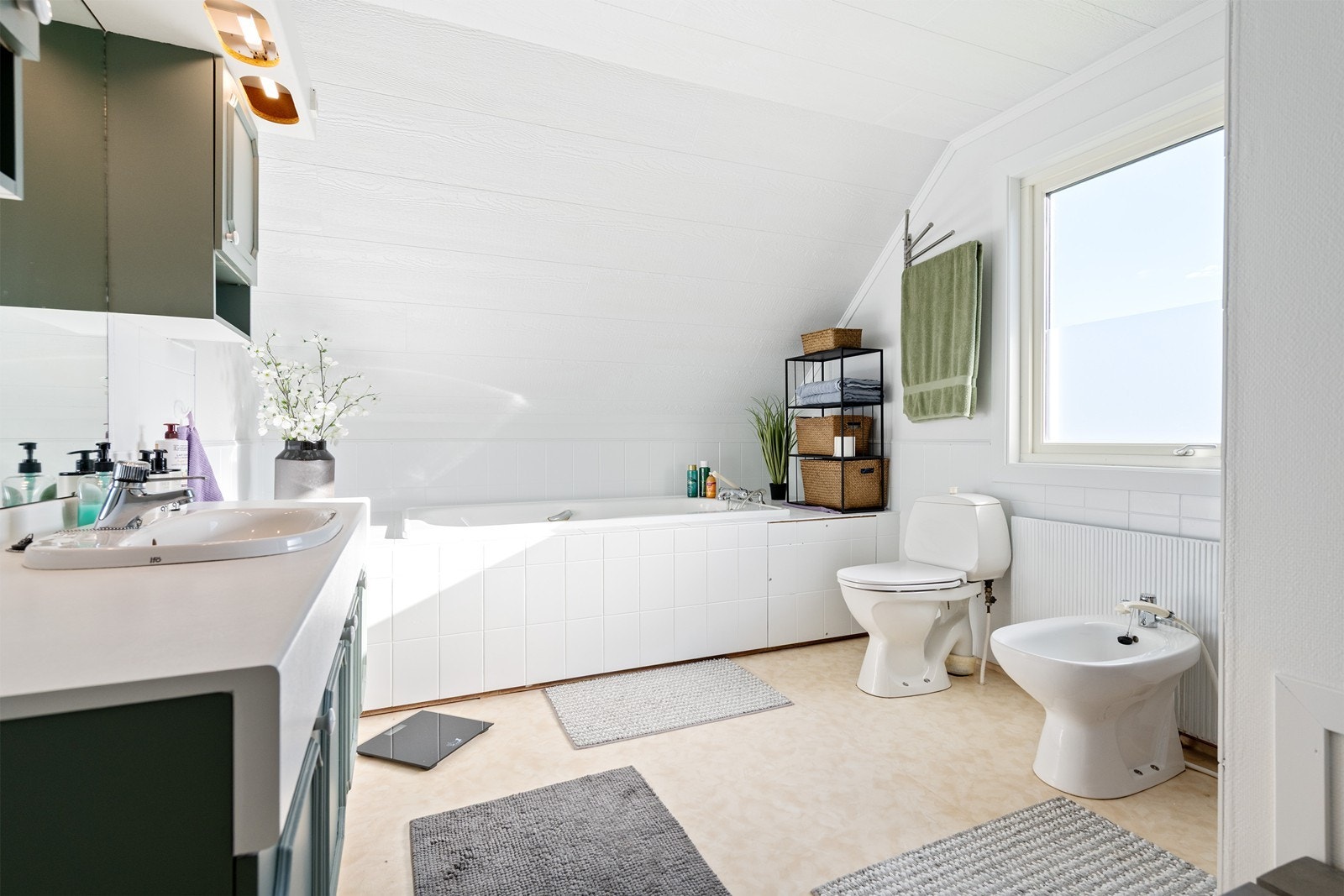 Bad med vaskeservant i innredning, gulvmontert wc, bide, innebygget badekar og dusjnisje.
Rommets innvendige overflater består av gulvbelegg på gulv, fliser og slette malte flater på vegg og slette malte flater i tak. Galleribilde