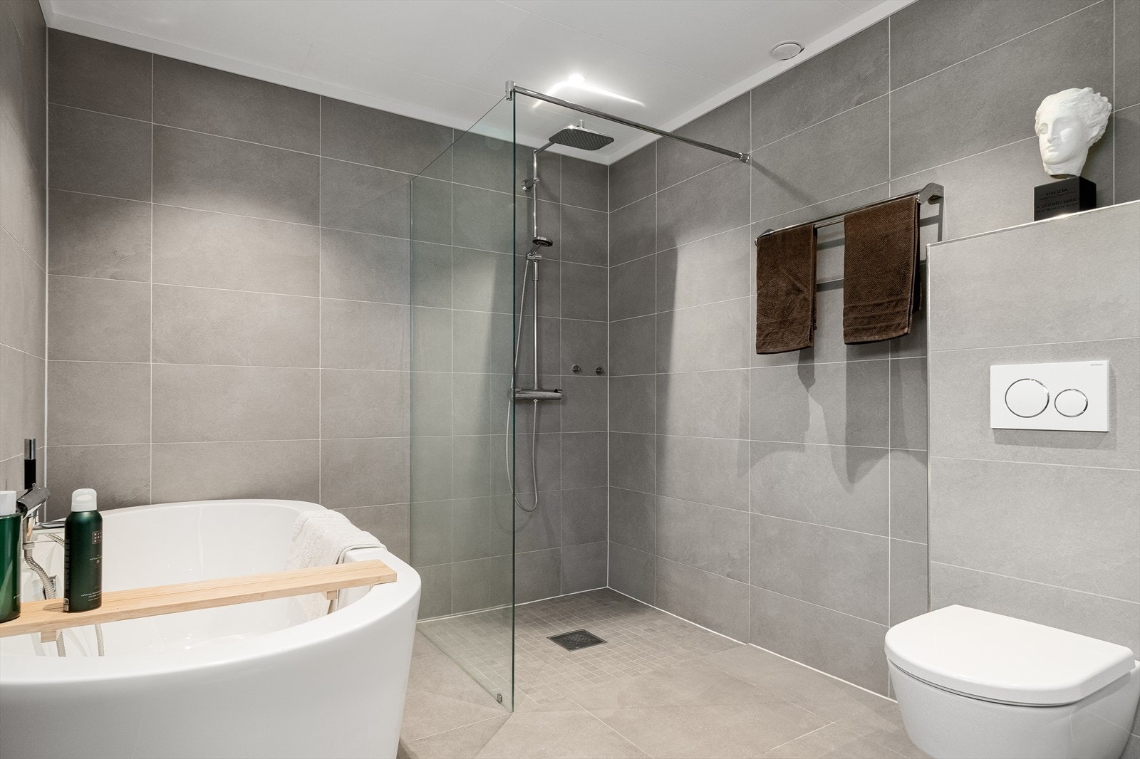 Bad i underetasje er innredet med badekar, vegghengt dusj med skjermvegg i herdet glass og veggmontert toalett med innebygget sisterne. Galleribilde