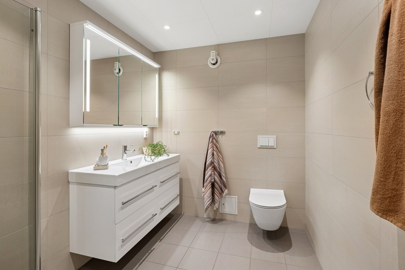 Badet er utstyrt med servant med underskap, speil med tilhørende belysning, dusjvegger og vegghengt wc. Det er mekanisk avtrekk og tilluft ved dør. Galleribilde