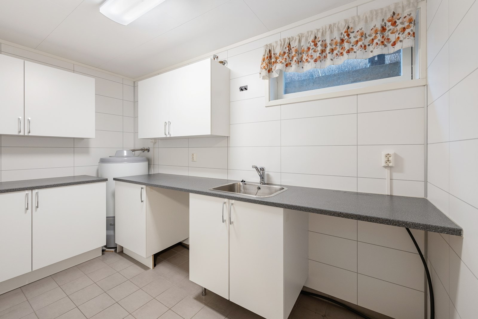 Separat vaskerom med baderomsplater på vegg, fliser på gulv og himlingsplater i taket. Rommet er utstyrt med opplegg for vaskemaskin og utslagsvask. Det er naturlig ventilering. Galleribilde