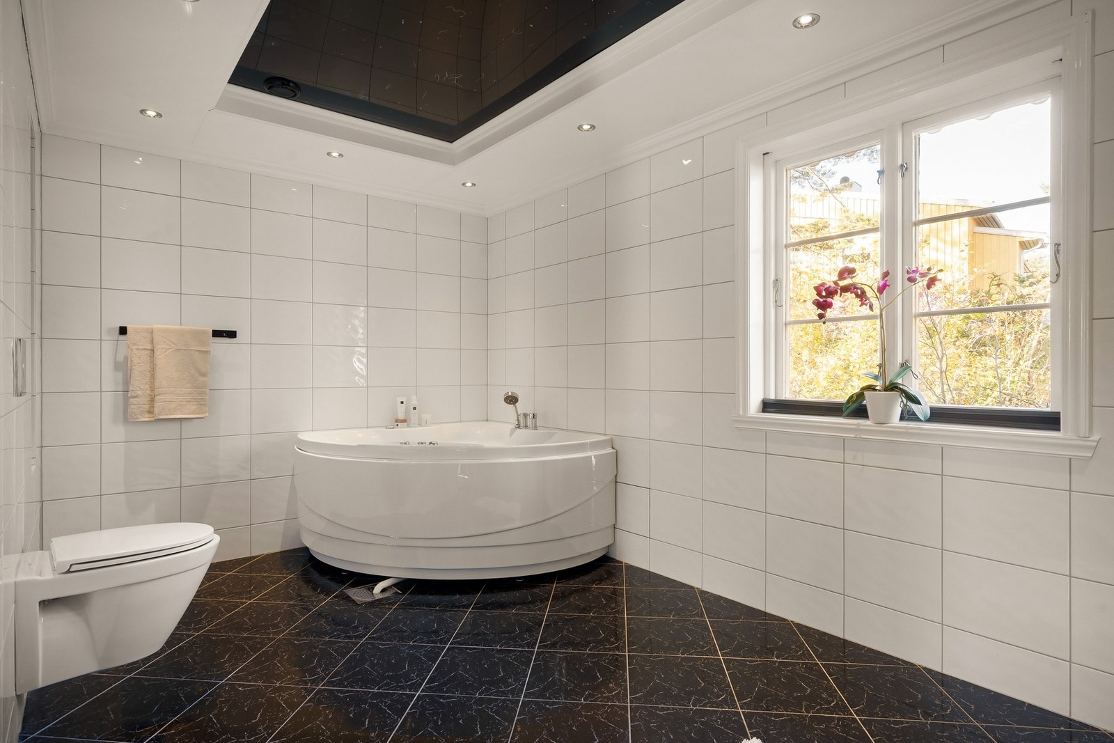 Delikat og flislagt bad med badekar og vegghengt toalett. Galleribilde