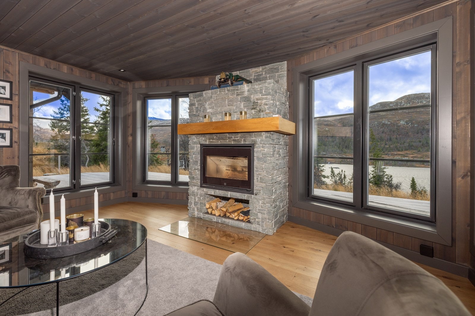 Romslig stue med omkransede, store vindusflater som inviterer naturen inn i rommet Galleribilde