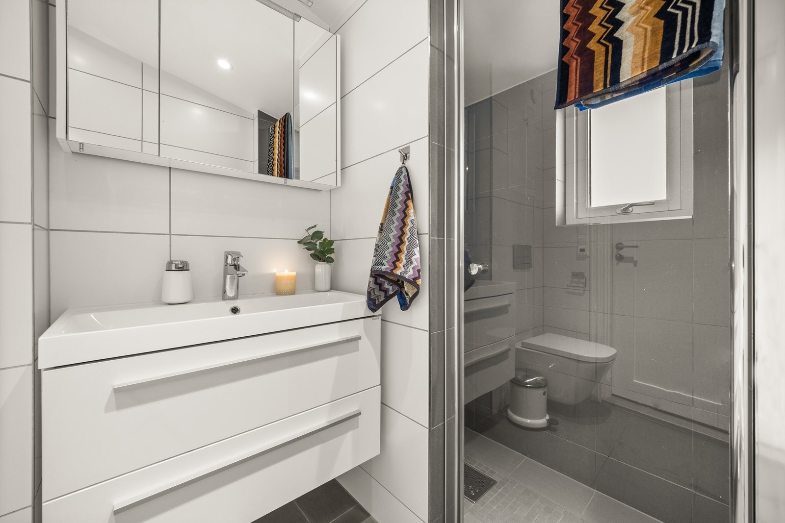 Badet er innredet med servantskap med nedfelt servant, speilskap med lys, veggmontert toalett med innebygd sisterne og dusjsone med dusjdør i herdet glass. Galleribilde