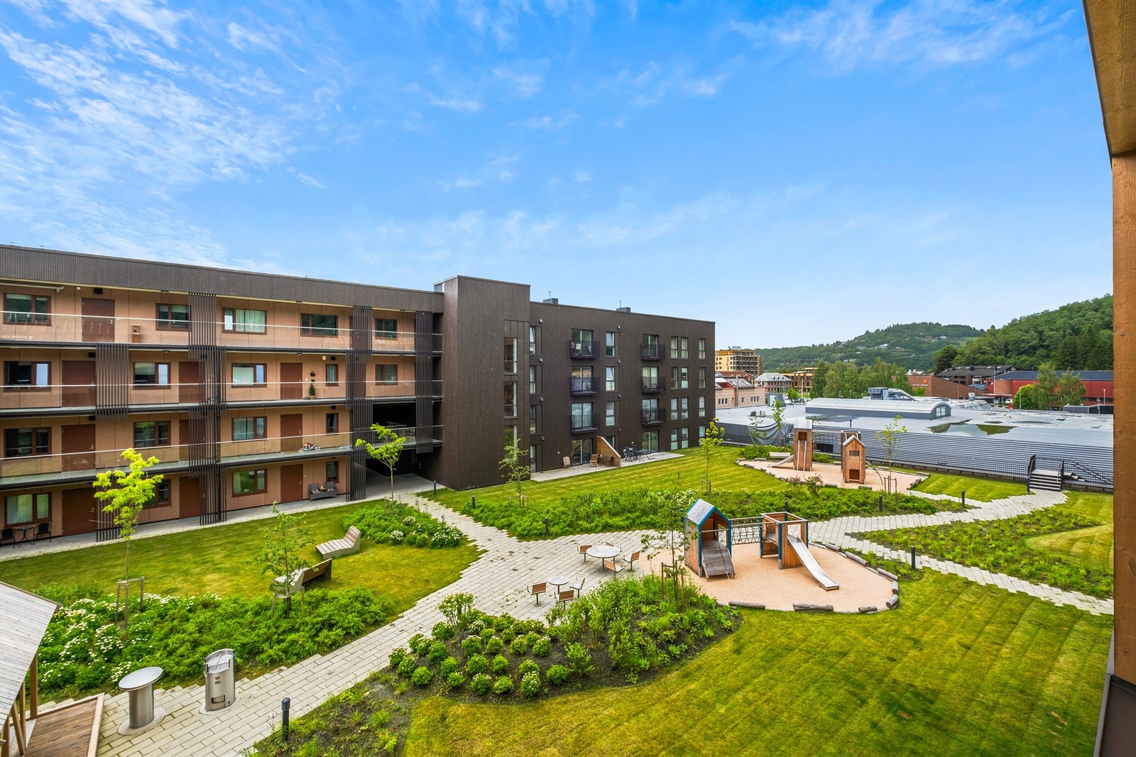 Utsikten fra balkongen over fellesområde med lekeplass og grønne omgivelser. Galleribilde