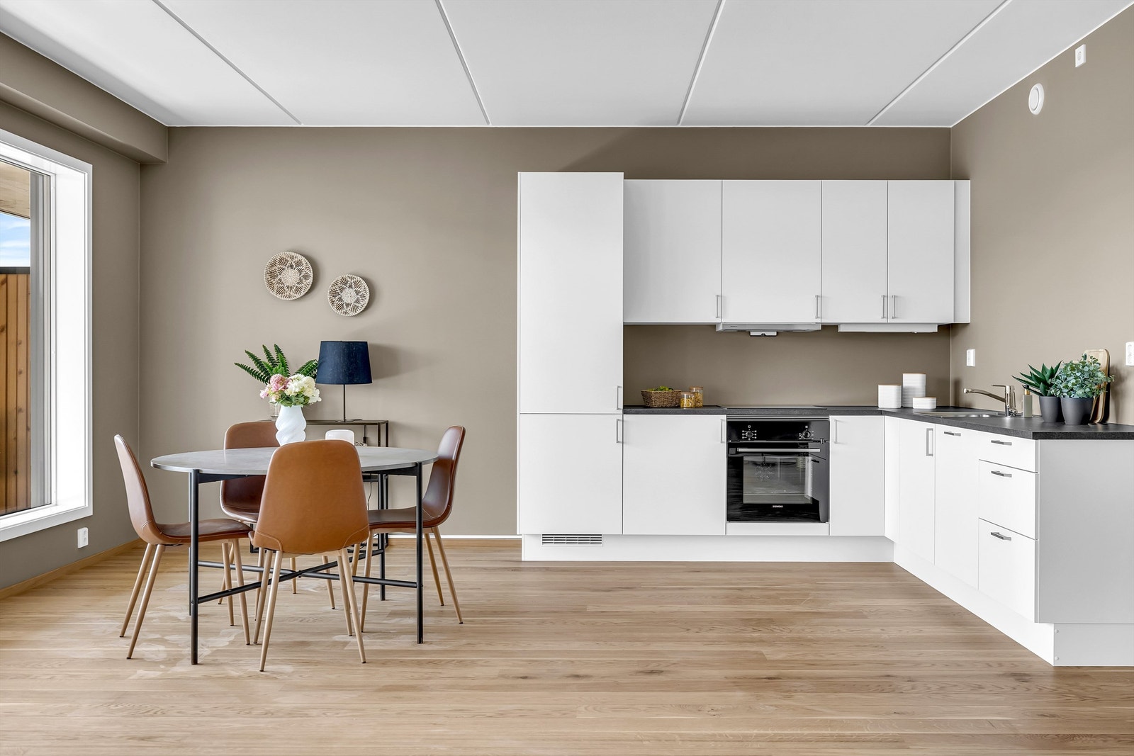 Stilrent kjøkken med hvite fronter og svart benkeplate, kombinert med et koselig spiseområde og dekorative detaljer som skaper en varm og innbydende atmosfære Galleribilde