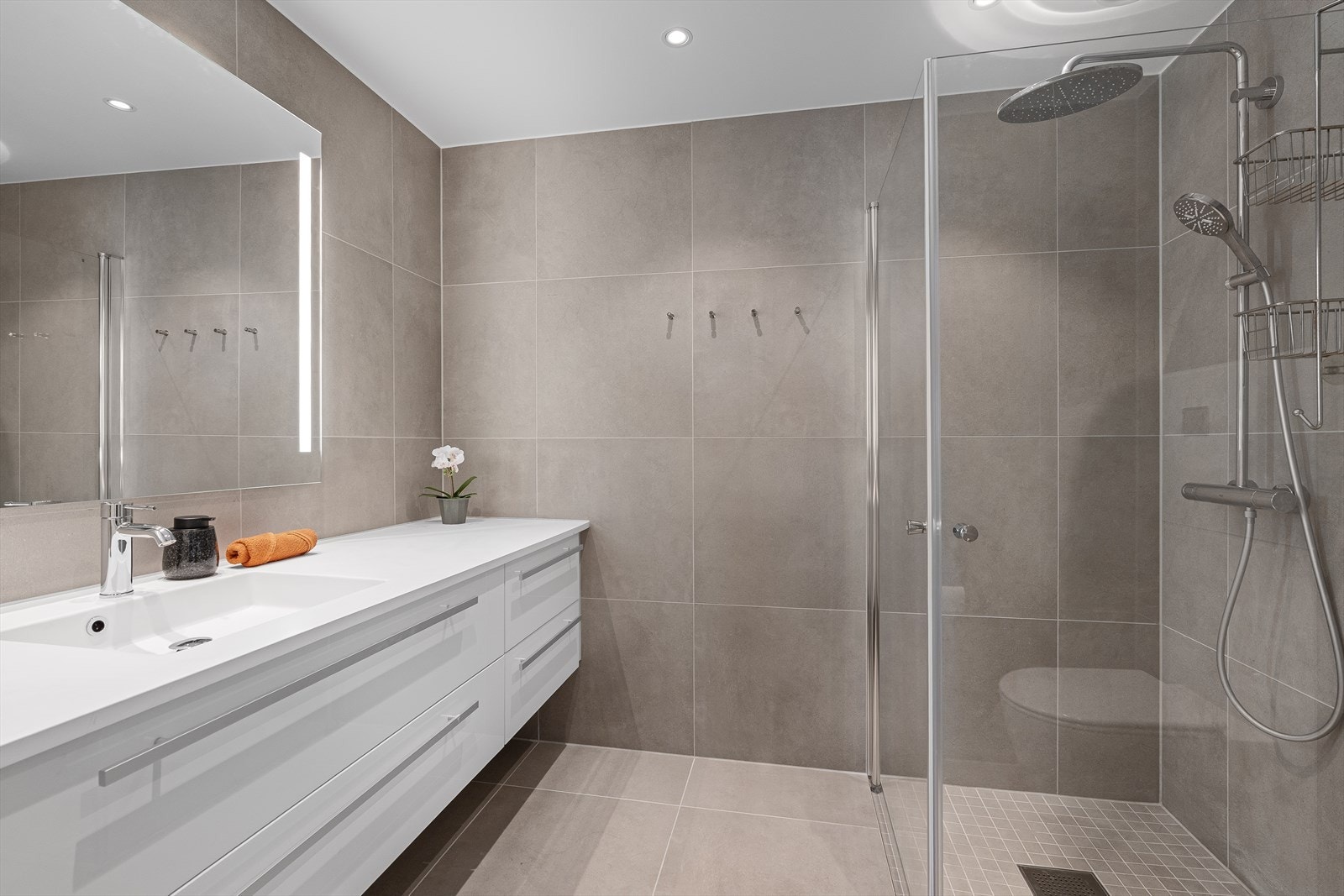 Badet er helfliset med varme i gulvet. Det inneholder en dusjnisje med innfellbare dusjdører og regndusj, vegghengt toalett, samt baderomsinnredning med speil over. Det er forøvrig downlights i himlingen. Galleribilde