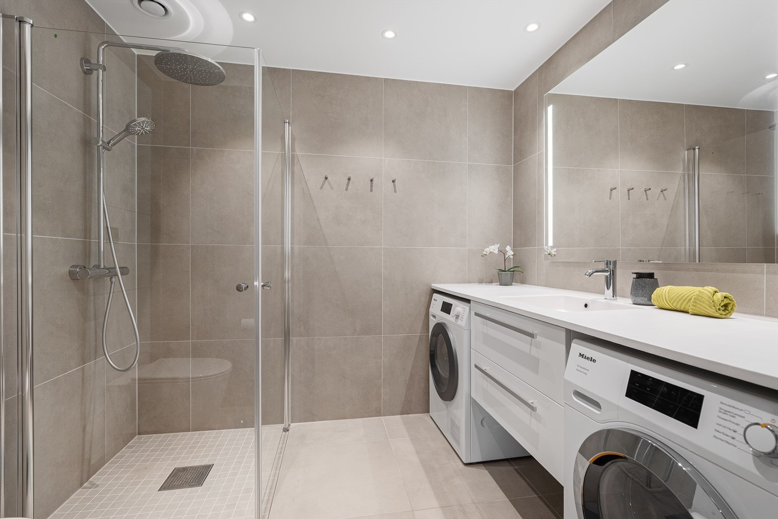 Bad nr. 2 inneholder en baderomsinnredning med avsatt plass til vaskemaskin og tørketrommel, vegghengt toalett, samt dusjnisje med innfellbare dusjdører og regndusj. Downlights i himling. Galleribilde