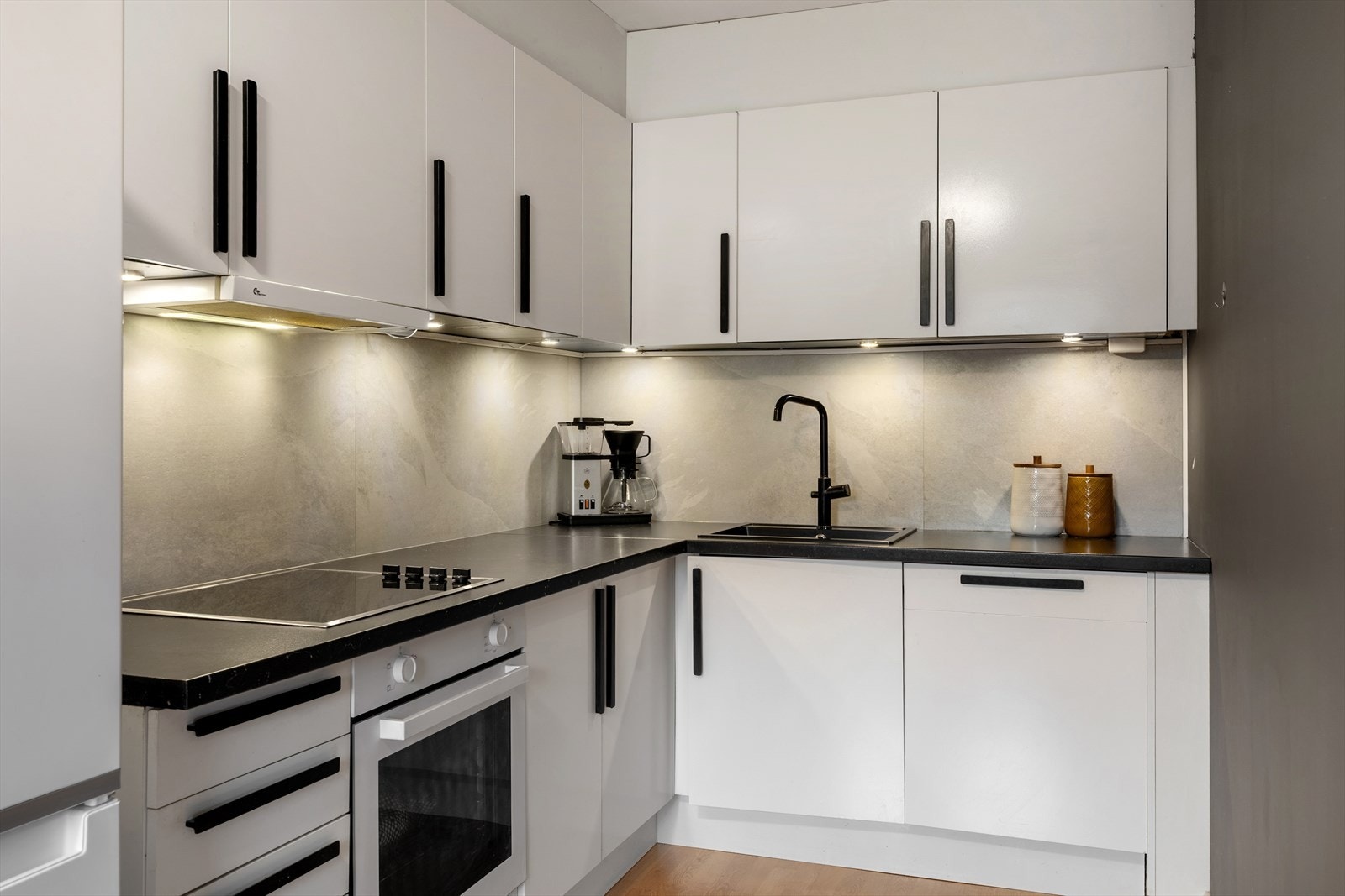 Kjøkkenet har en praktisk utforming med innredning i hvit utførelse, sorte håndtak og laminert benkeplate. Det er integrert stekeovn, platetopp og oppvaskmaskin, samt ventilator med kullfilter. Galleribilde