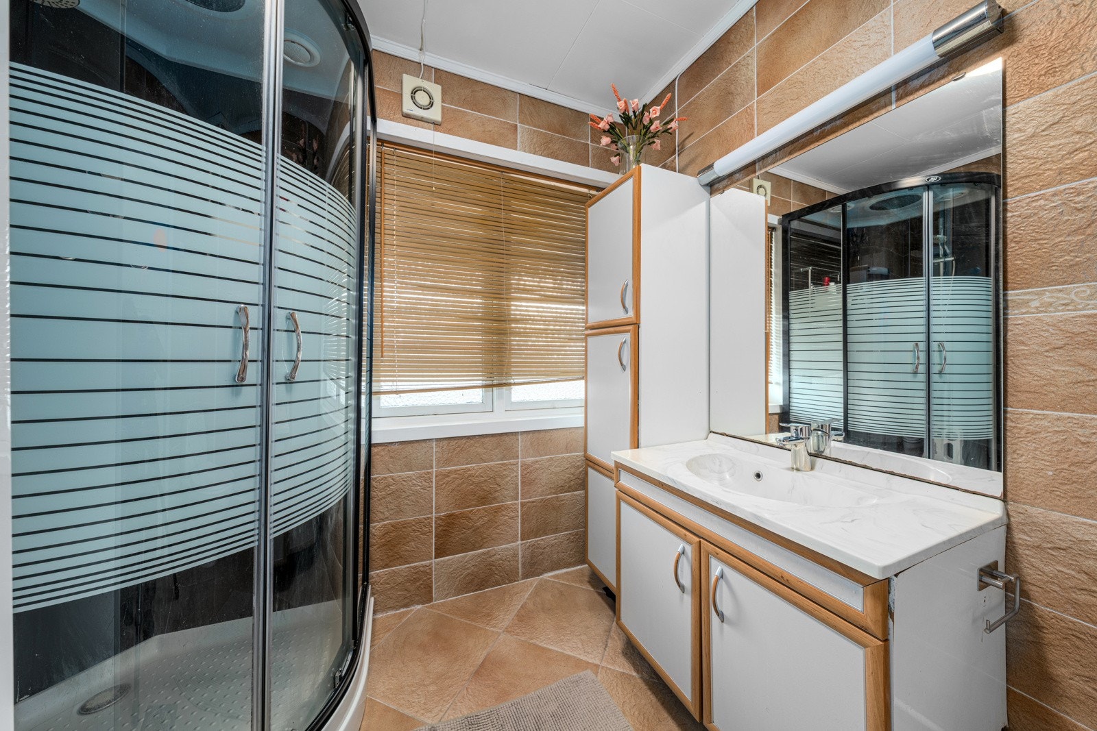 Bad med beige fliser, lys servant og praktisk sideskap som gir ekstra oppbevaringsplass. Galleribilde