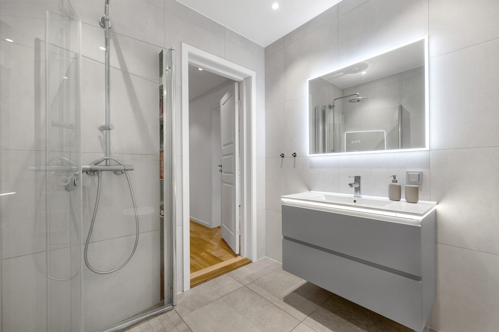 Moderne baderomsinnredning med heldekkende servant. Badet er blant annet utstyrt med opplegg for vaskemaskin, praktiske innfellbare dusjdører, veggmontert wc mm. Galleribilde