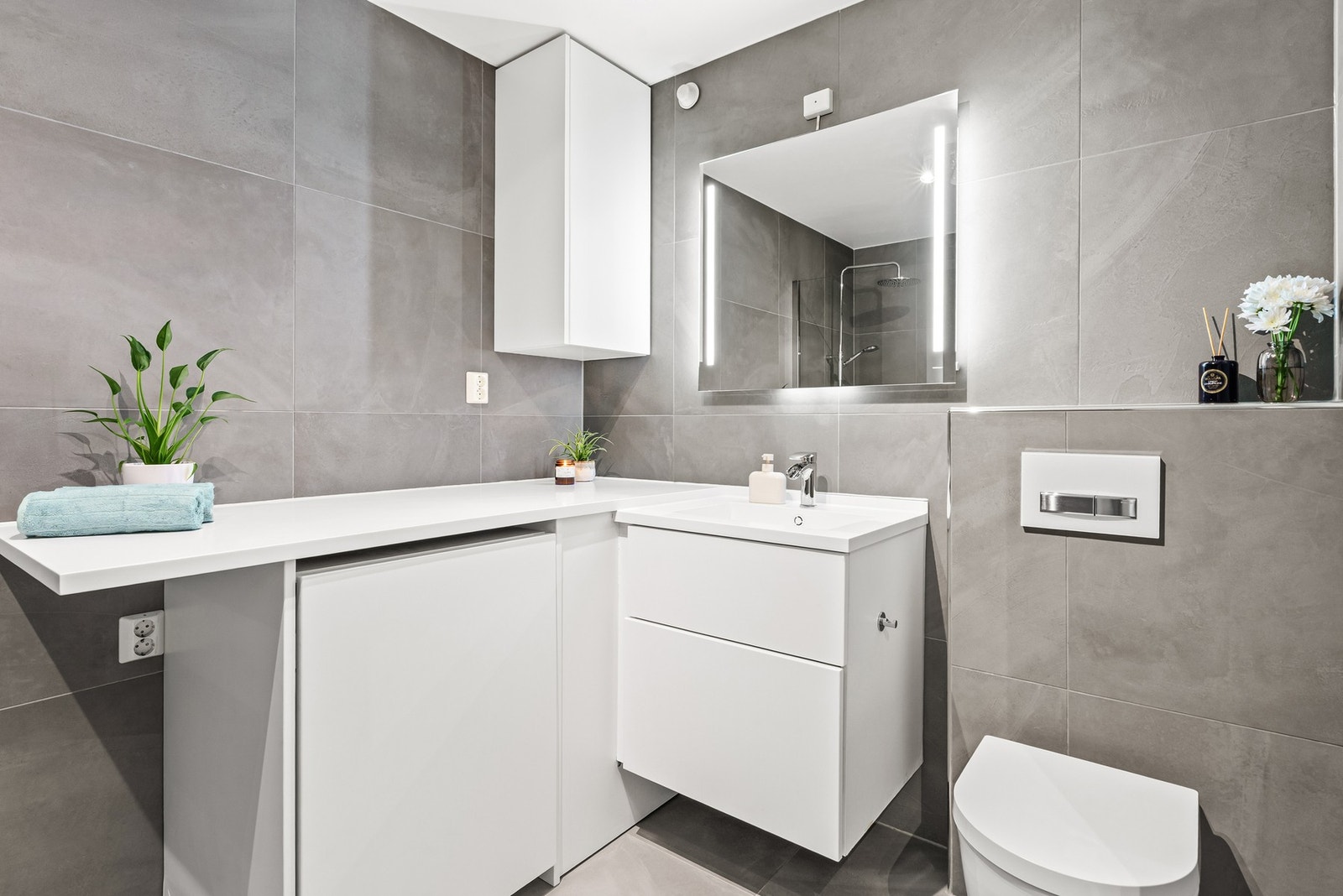 Baderomsinnredningen har hvite, glatte fronter og består av en heldekkende servant på en skuffeseksjon, et veggskap, et høyskap, en benkeseksjon og et speil med integrert belysning. Galleribilde