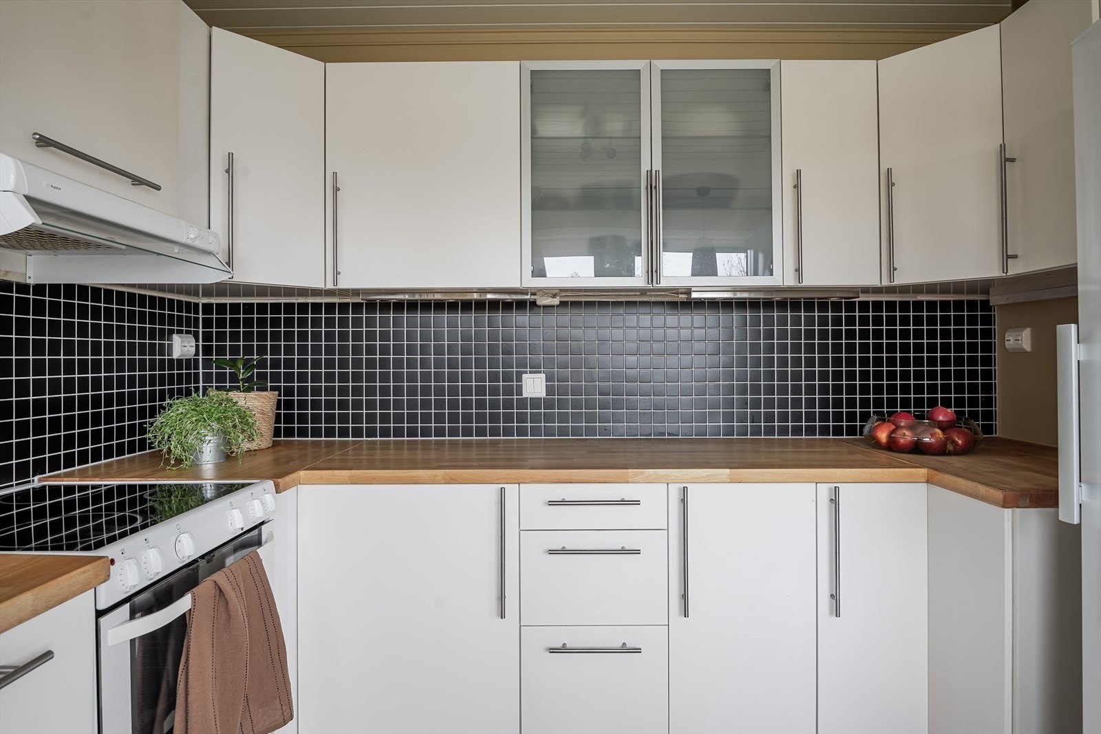 Lys og tidløs kjøkkeninnredning med glatte fronter og heltre benkeplate med nedfelt oppvaskkum. Praktisk med sorte fliser i benkeryggen og belysning under overskapene. Galleribilde