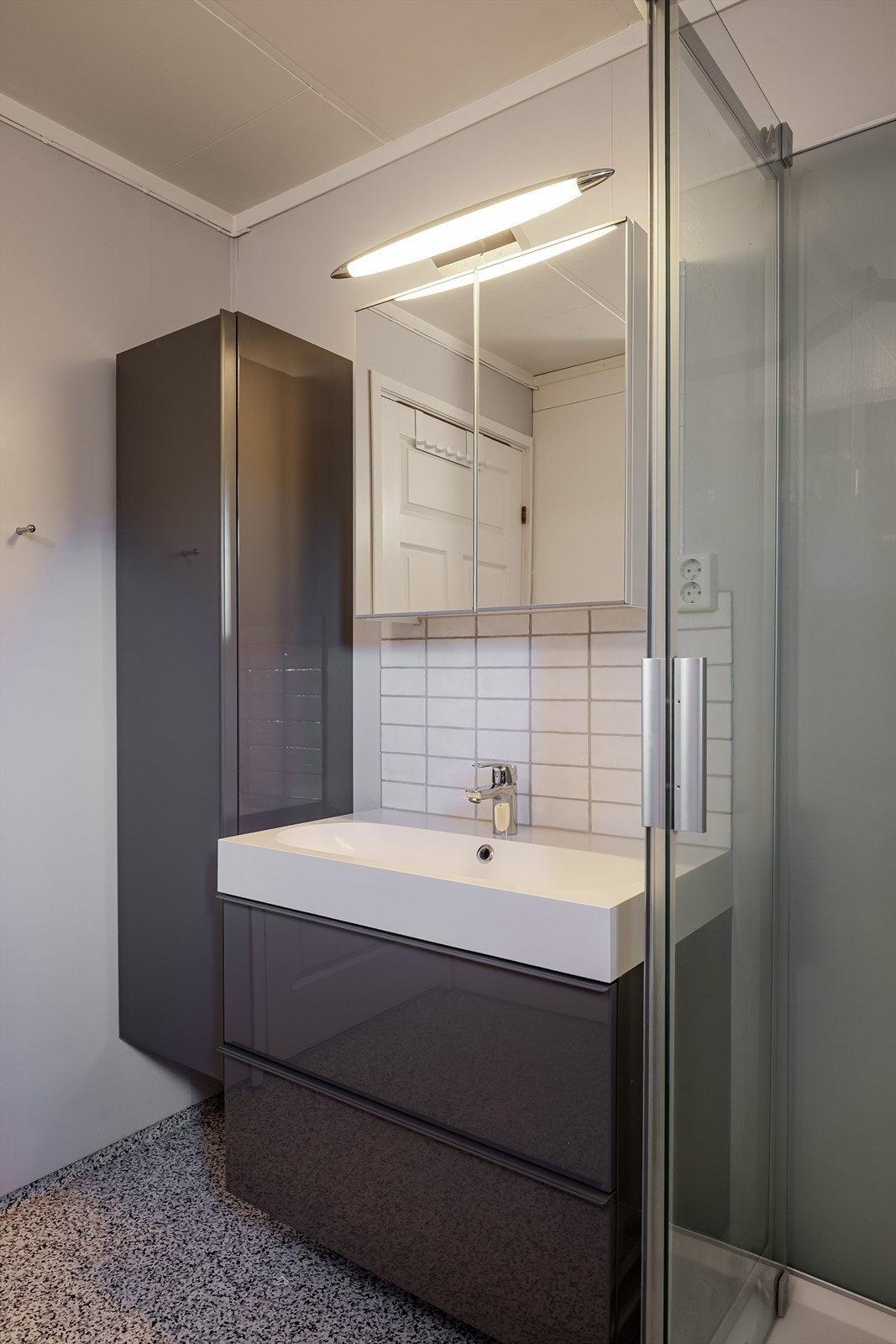 Moderne baderomsinnredning med skuffer og heldekkende servant med fliser over, vegghengt speilskap med overlys og ekstra høyskap ved siden av. Galleribilde