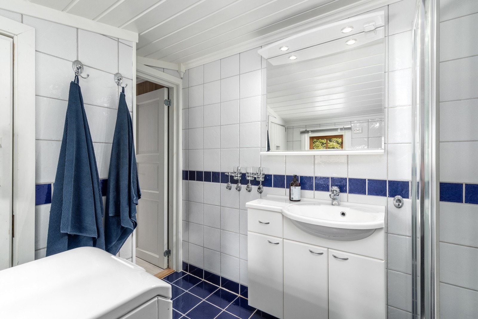 Badet er innredet med vegghengt servantinnredning, speil med overlys, dusjhjørne og gulvstående toalett Galleribilde