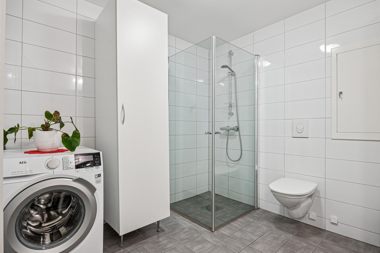 Badet er utstyrt med vegghengt servantinnredning, speil med lys og stikkontakt, dusjhjørne med glassdører, vegghengt toalett og opplegg for vaskemaskin. Galleribilde