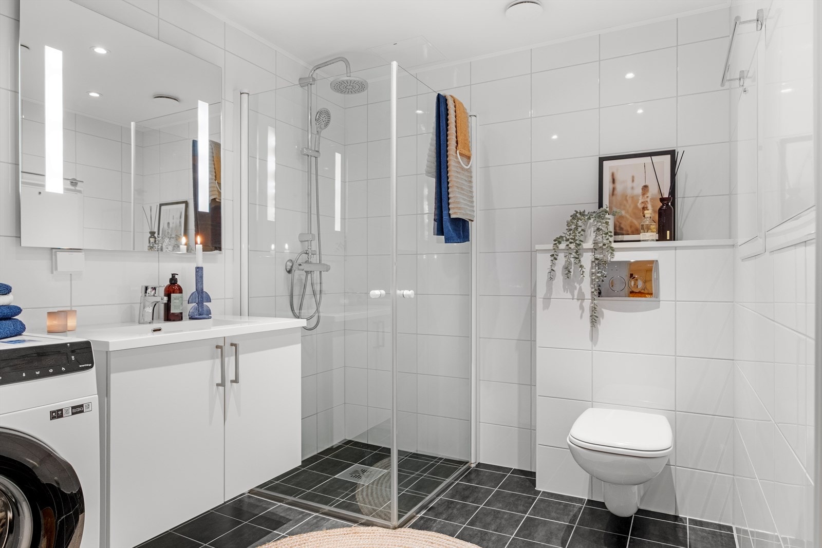 Her får du stort dusjhjørne, opplegg for vaskemaskin, servant med underskap, speil med integrert belysning og spotter i tak. Galleribilde