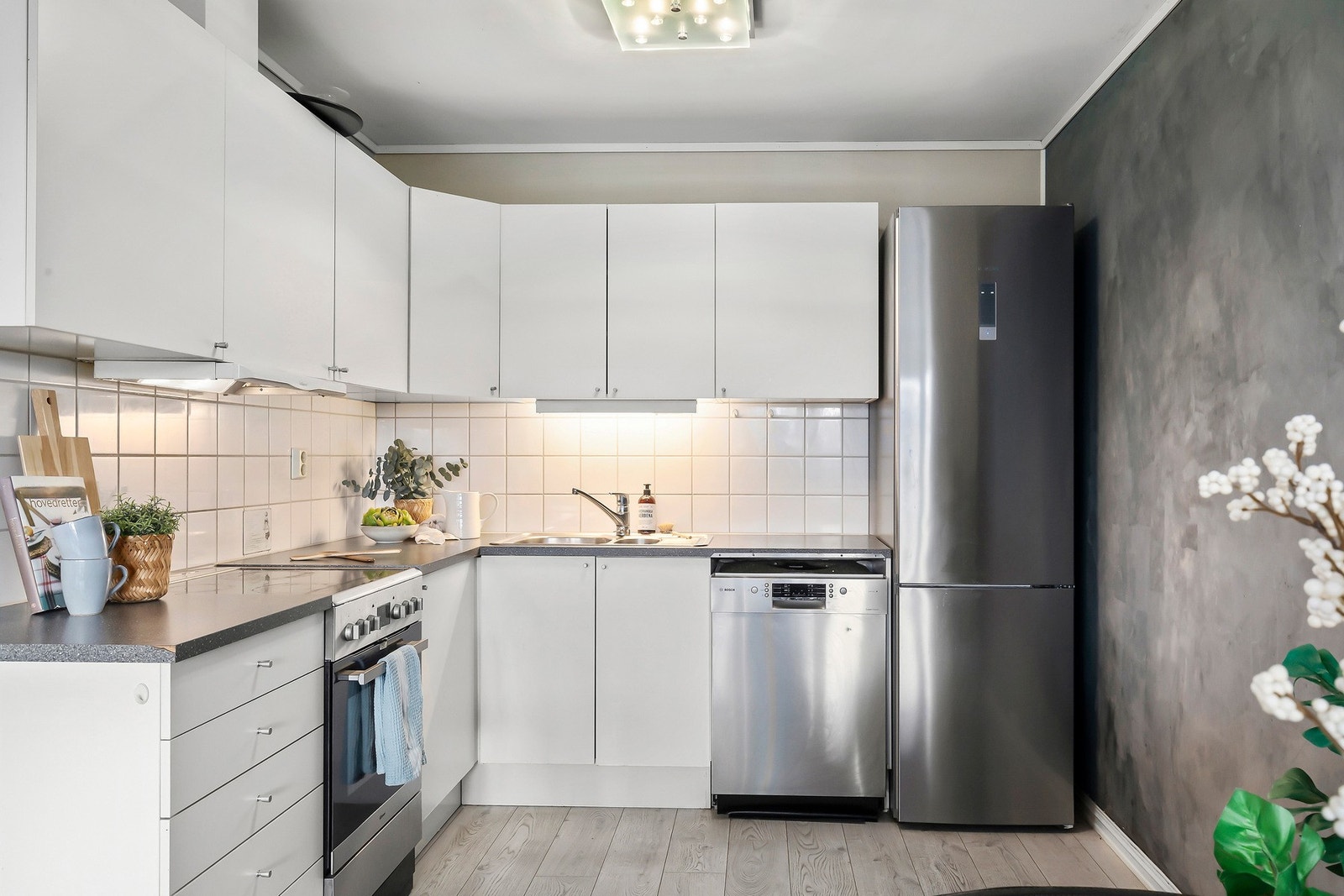 Det er flis på vegg over benkeplate, innredning med mekanisk avtrekksvifte over stekesonen, og opplegg for oppvaskmaskin. Galleribilde