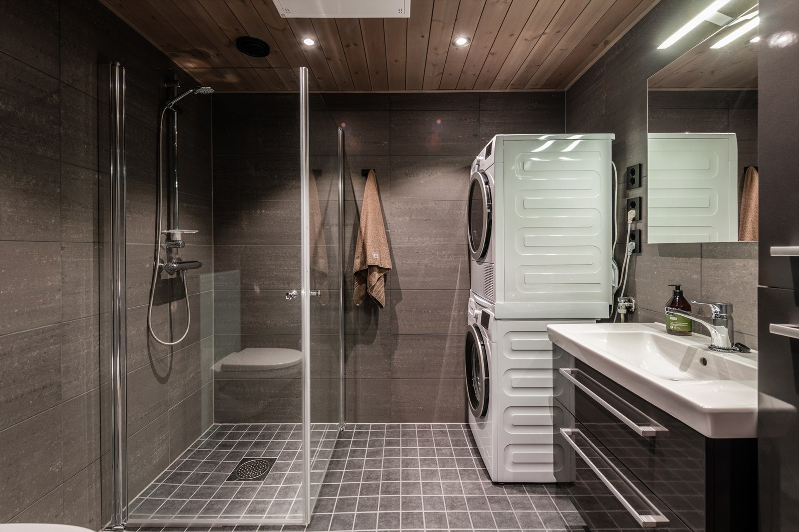 Lekkert bad med servantinnredning, dusjvegger i glass, vegghengt toalett og opplegg for vaskemaskin Galleribilde