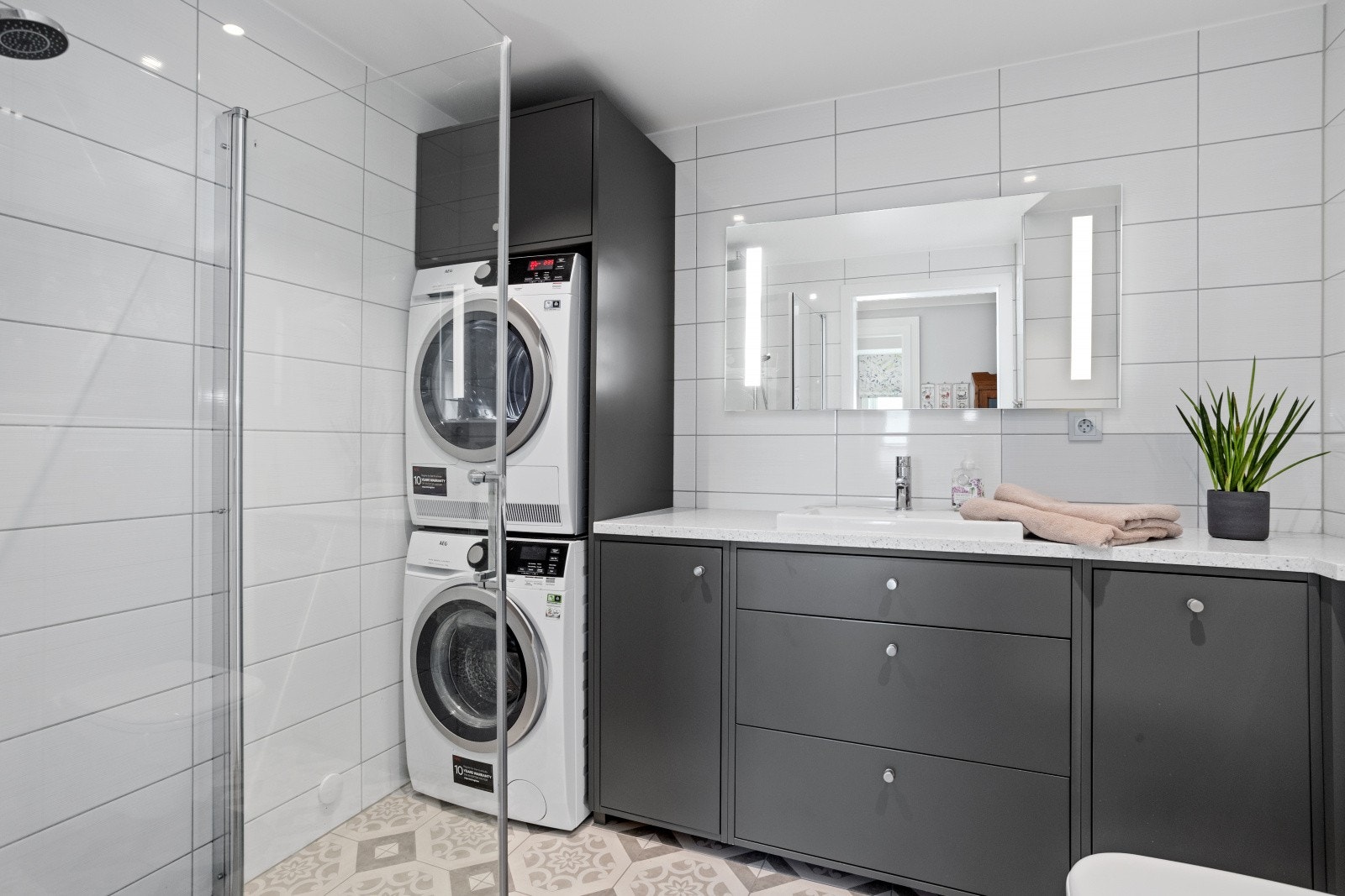 Vegghengt wc, dusjhjørne med glassvegger, plassbygget servantinnredning med Coran benkeplate og toppmontert servant (2020), speil med integrert belysning (2020). Blandebatteri i dusjsone fra 2020. Opplegg for vaskemaskin og tørketrommel i innredning. Galleribilde