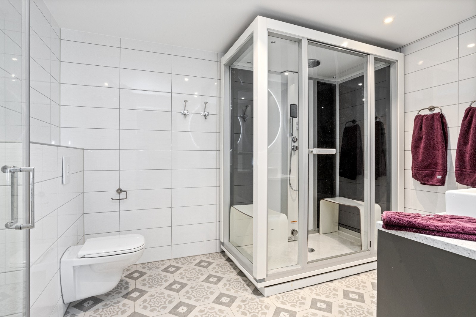 Lekkert flislagt bad med gulvvarme, downlights og integrert sononsanlegg fra byggeår. Vegghengt wc, frittstående steambadstue fra Tylø, dusjhjørne med nedsenket gulv og glassvegger, plassbygd servantinnredning med Coran benkeplate og toppmontert servant. Galleribilde