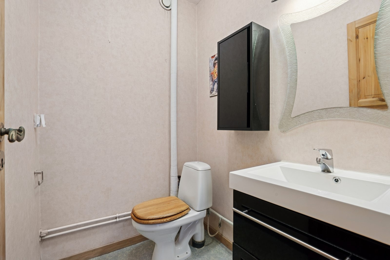 Separat WC-rom ved siden av baderom. Gulvet er belagt med vinylbelegg, vegger med tapet og overflate himling med malt betong. Galleribilde