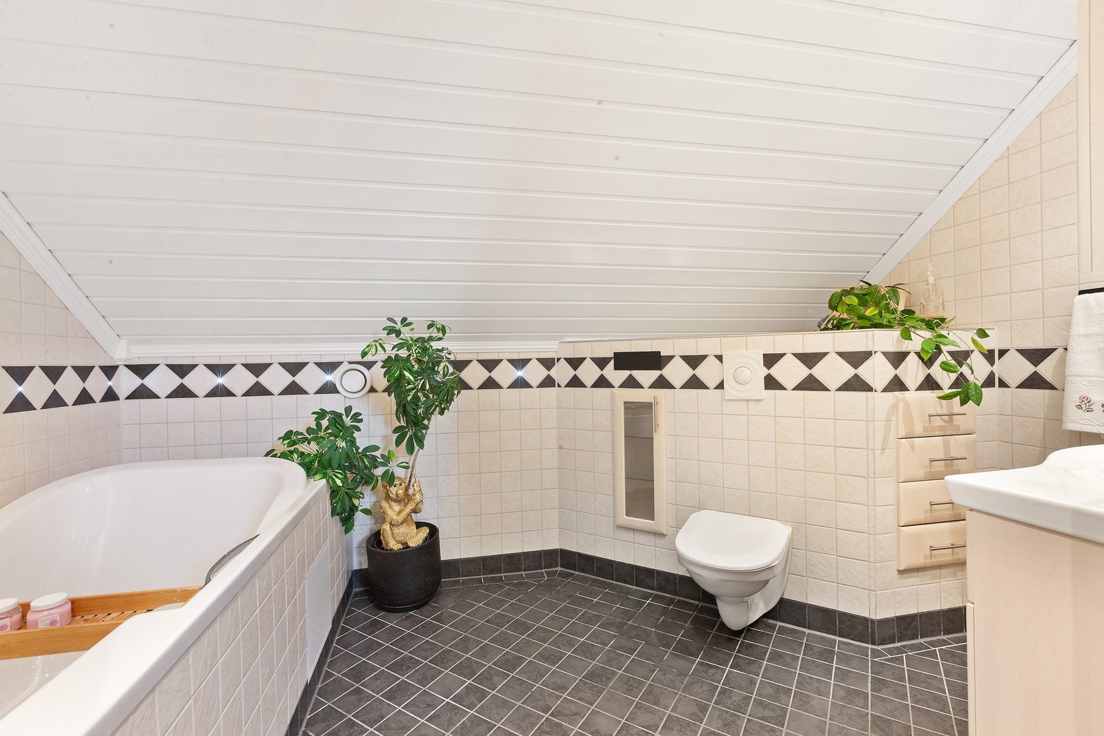 Badet har lys innredning, badekar og vegghengt toalett, hjørnet utnyttes smart med funksjonelle skuffer og skap. Varme i gulv. Galleribilde