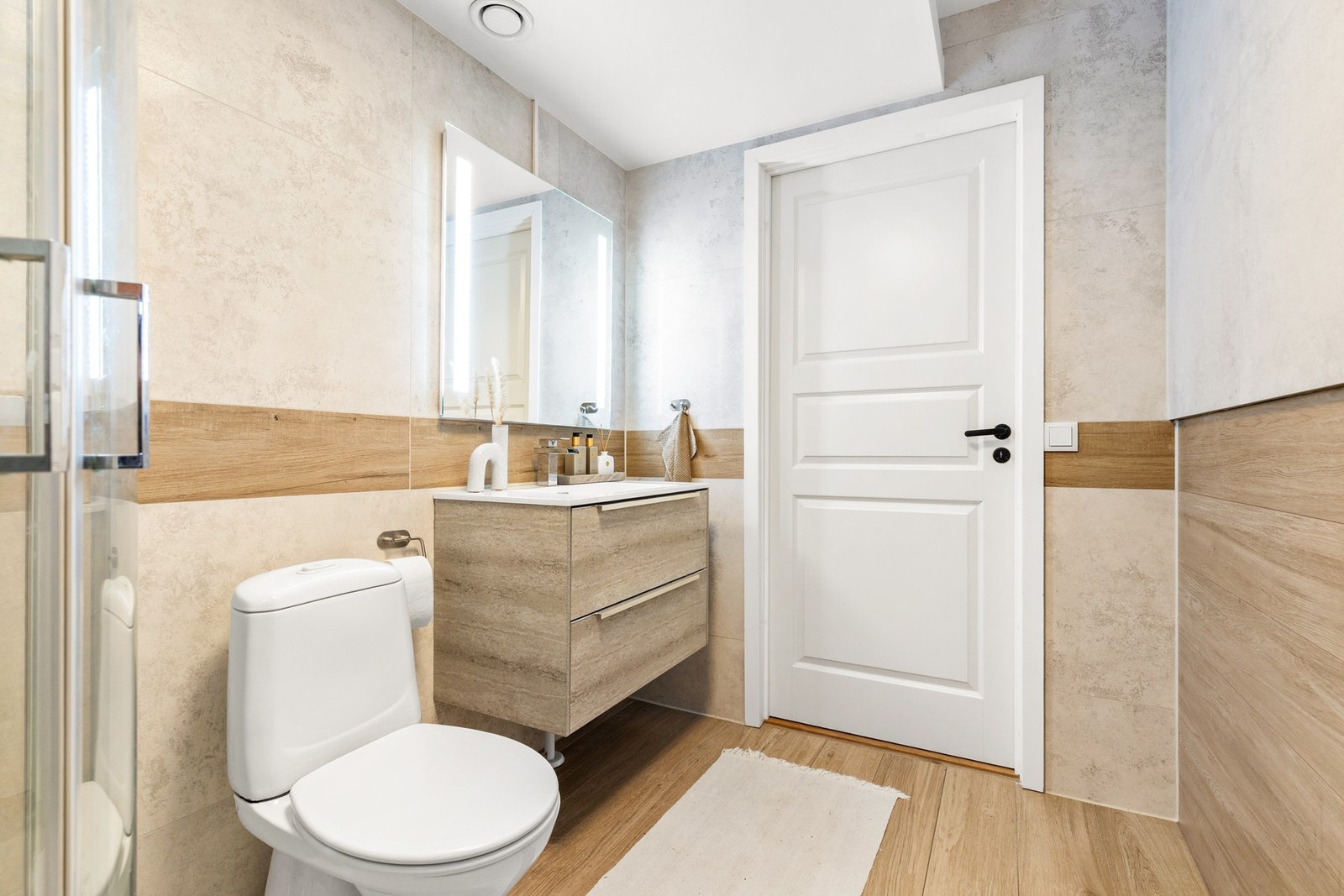 Badet er er innredet med gulvstående toalett, dusjkabinett, servantinnredning og speil med integrert belysning Galleribilde