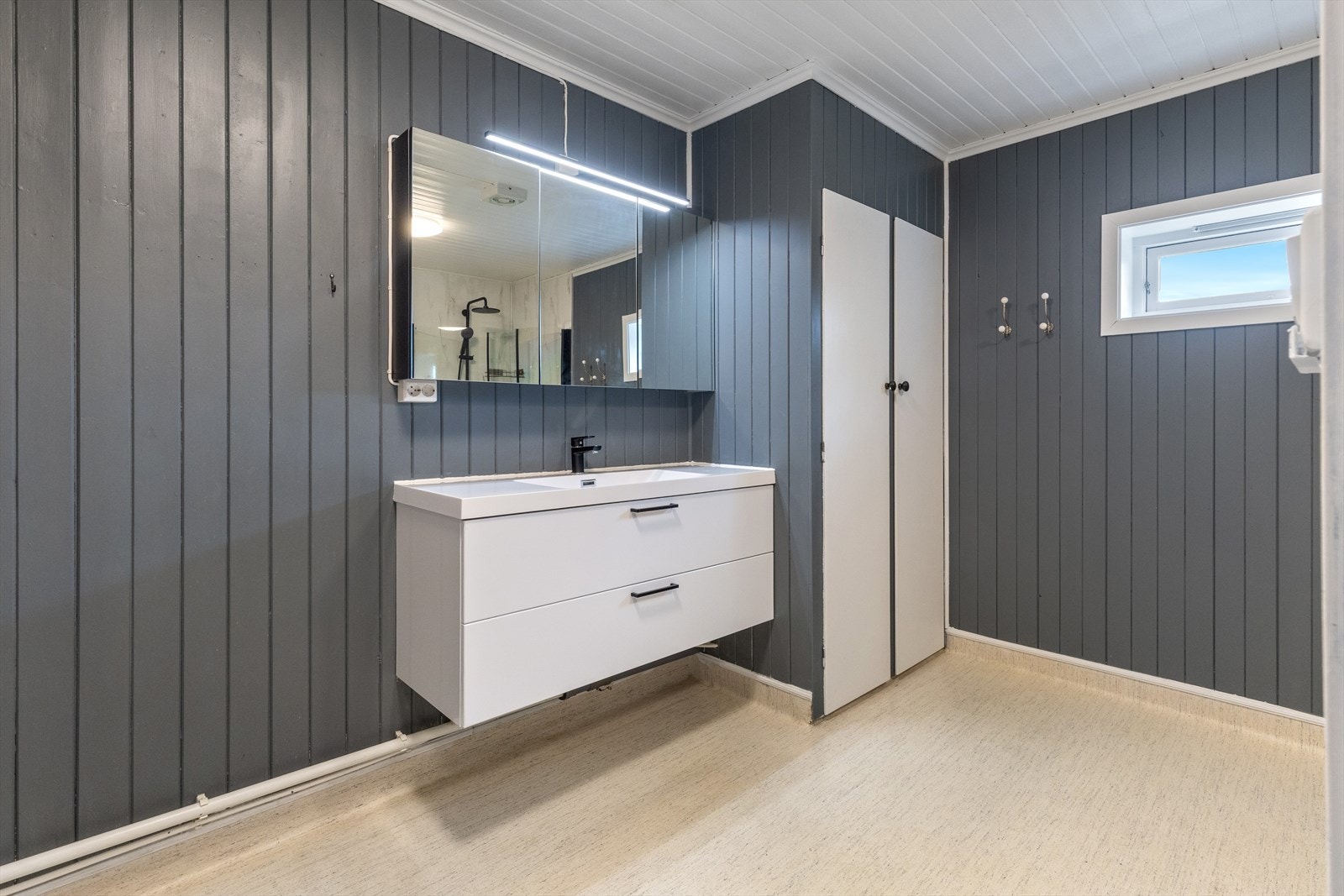 Badet har servant i servantskap med store skuffer, speil med lampe over servant og plassbygget skap ved siden av servantinnredning. Galleribilde