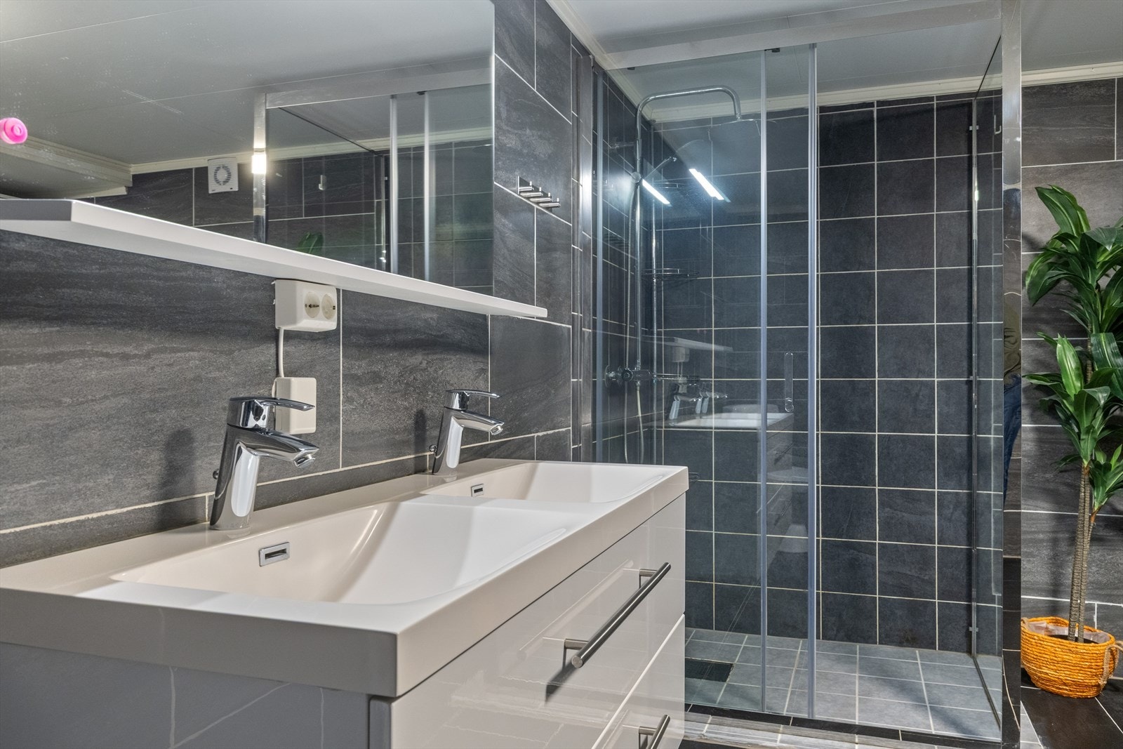 Badet har dobbel servant i servantskap med skuffer og speil med hylle og lys over. Dobbelt jordet strømuttak plassert under hylle. Galleribilde