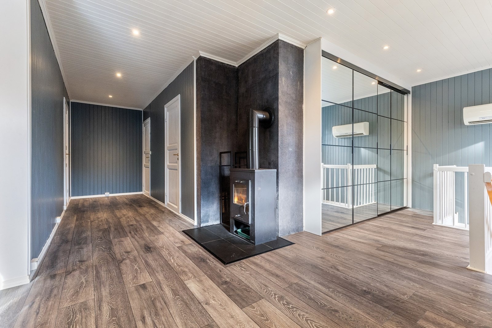 Lys og romslig gang/entre i 1. etasje med stor skyvedørsgarderobe og peisovn i hjørnet av gangen mot soverommene. Galleribilde