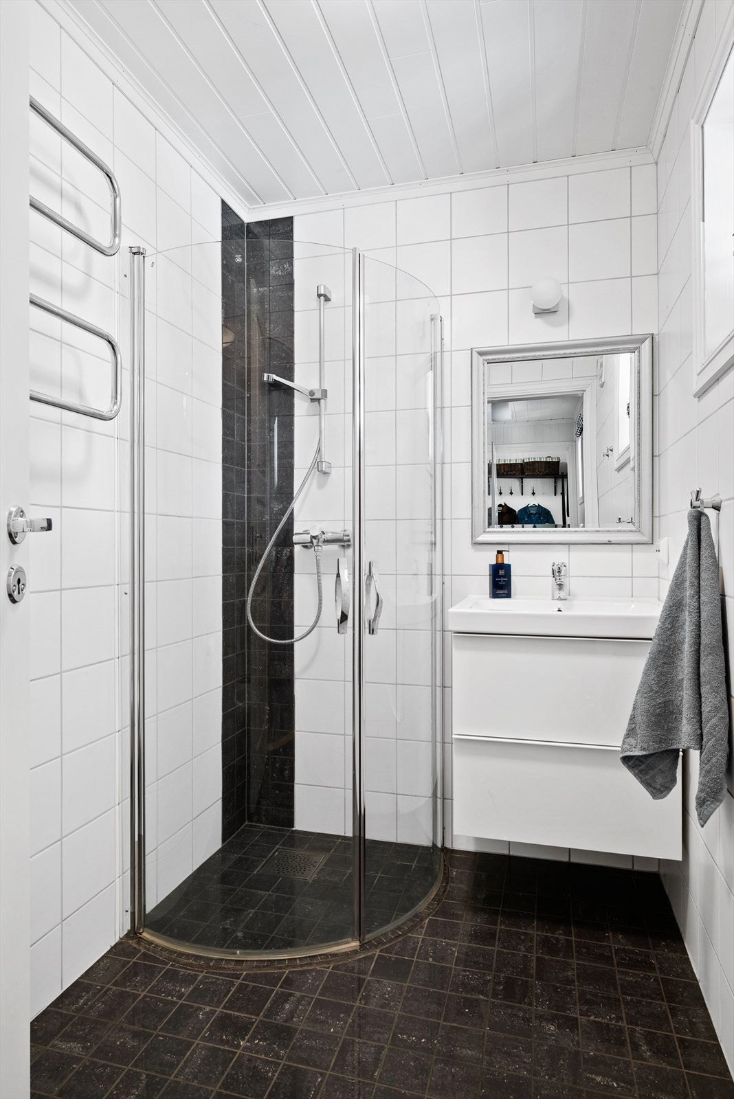 I gangen i 1. etasje får vi også et praktisk bad. Flis på gulv og flis på vegger. Malt panel i himling. Gulvvarme. Utstyrt med servantskap, mekanisk avtrekk, innfellbare dusjdører og veggmontert wc. Galleribilde