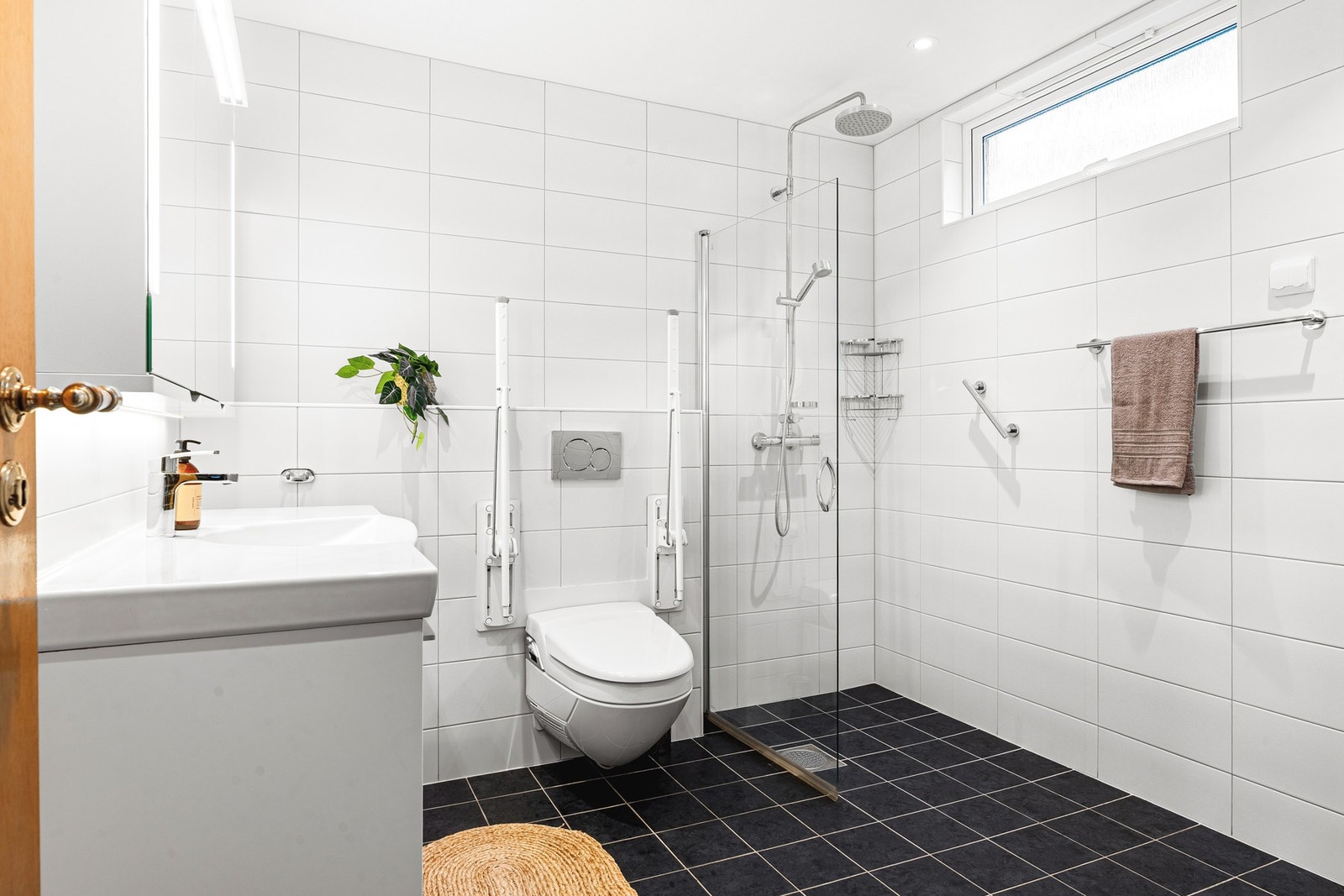 Badet er innredet med vegghengt toalett, baderomsinnredning, dusj m/glassvegger og opplegg for vaskemaskin. Galleribilde