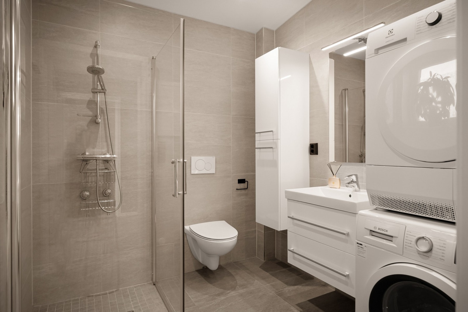 Flislagt bad/vaskerom med innredning, dusjhjørne, vegghengt toalett og opplegg for vaskemaskin. Galleribilde