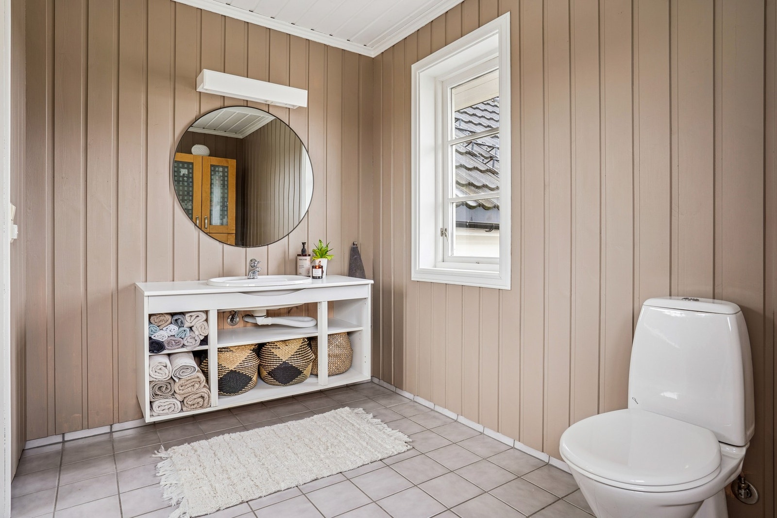 Badet fremstår som lyst og praktisk, med flislagt gulv, malt panel på vegger og i tak. Galleribilde