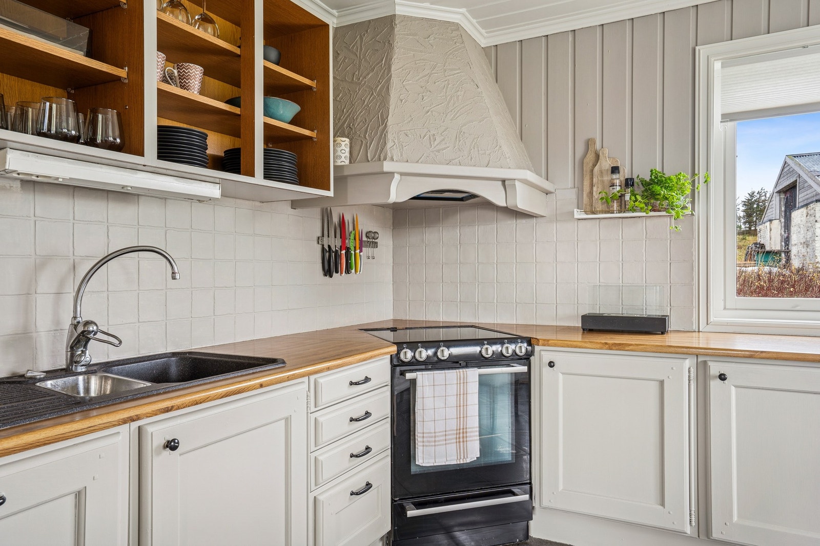 Rommet har flislagt gulv, malt panel på vegger og downlights i tak, som gir et moderne og pent uttrykk. Innredningen har malte profilerte fronter og laminat benkeplater, med god plass til både oppbevaring og matlaging. Galleribilde