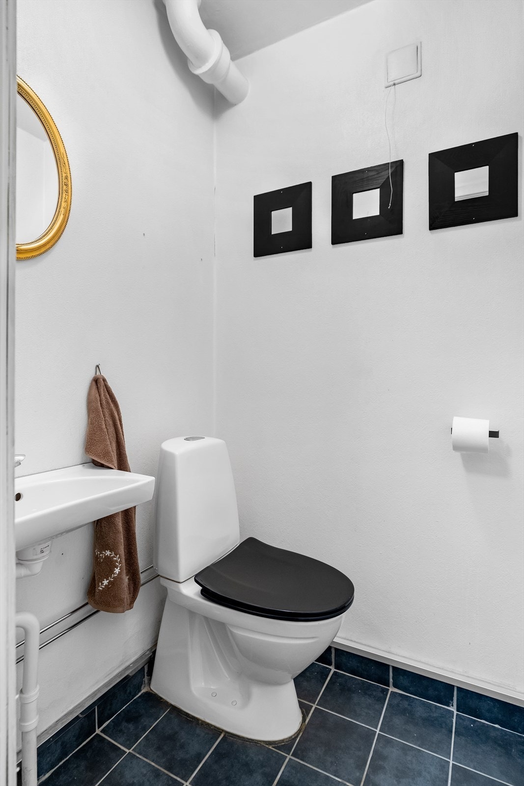 Vegg i vegg med badet ligger et toalettrom. Rommet har fliser på gulv, samt malte tapetserte veggflater. Videre er rommet innredet med vannklosett, servant, speil og lys. Galleribilde