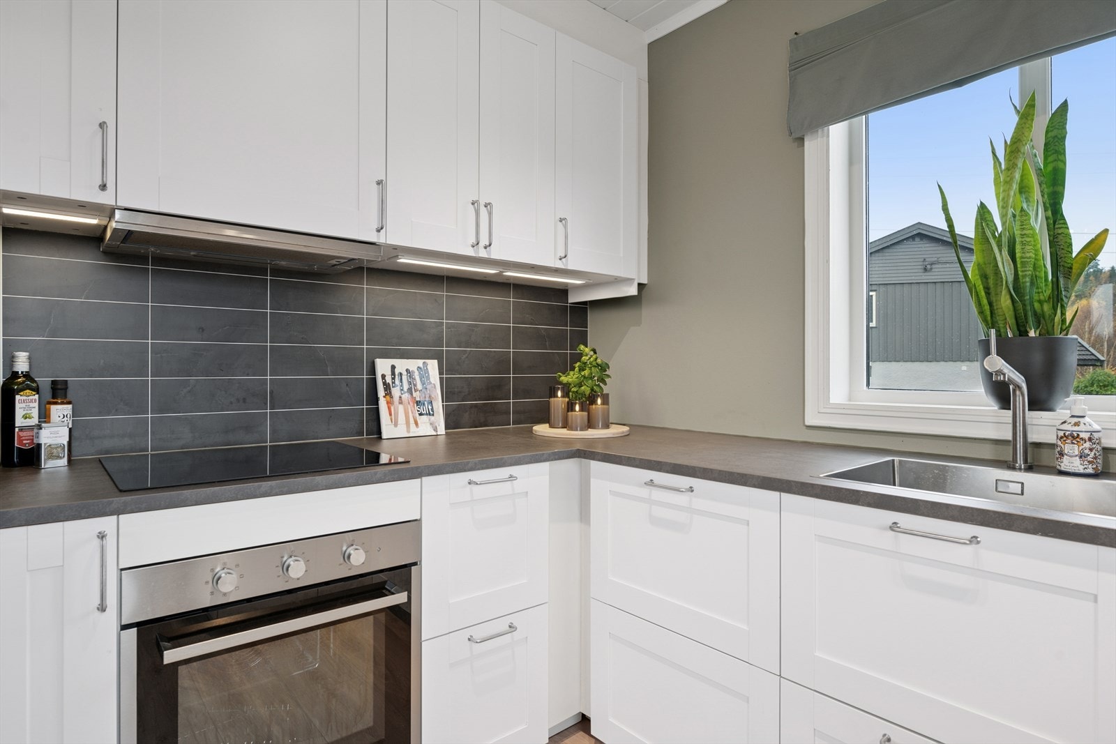 Det er laminatplate på vegg over benkeskap og belysning under overskap. Galleribilde