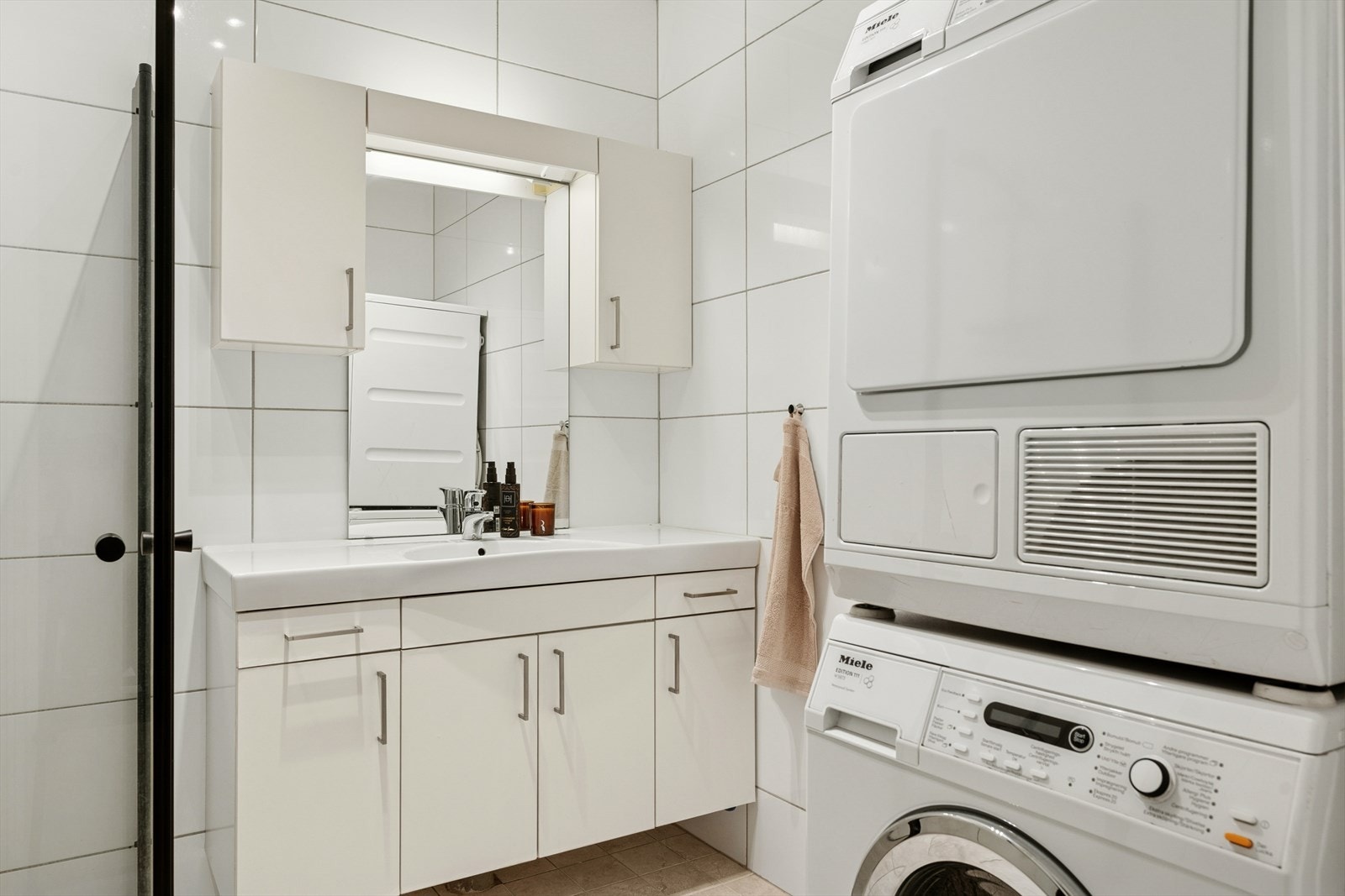 Baderomsinnredningen består av benkeskap og veggskap med glatte fronter, speil og belysning over servant. Videre er badet utstyrt med veggfestet klosett med innebygget sisterne, dusj med innfellbare vegger i herdet glass og servant i helstøpt plate. Galleribilde