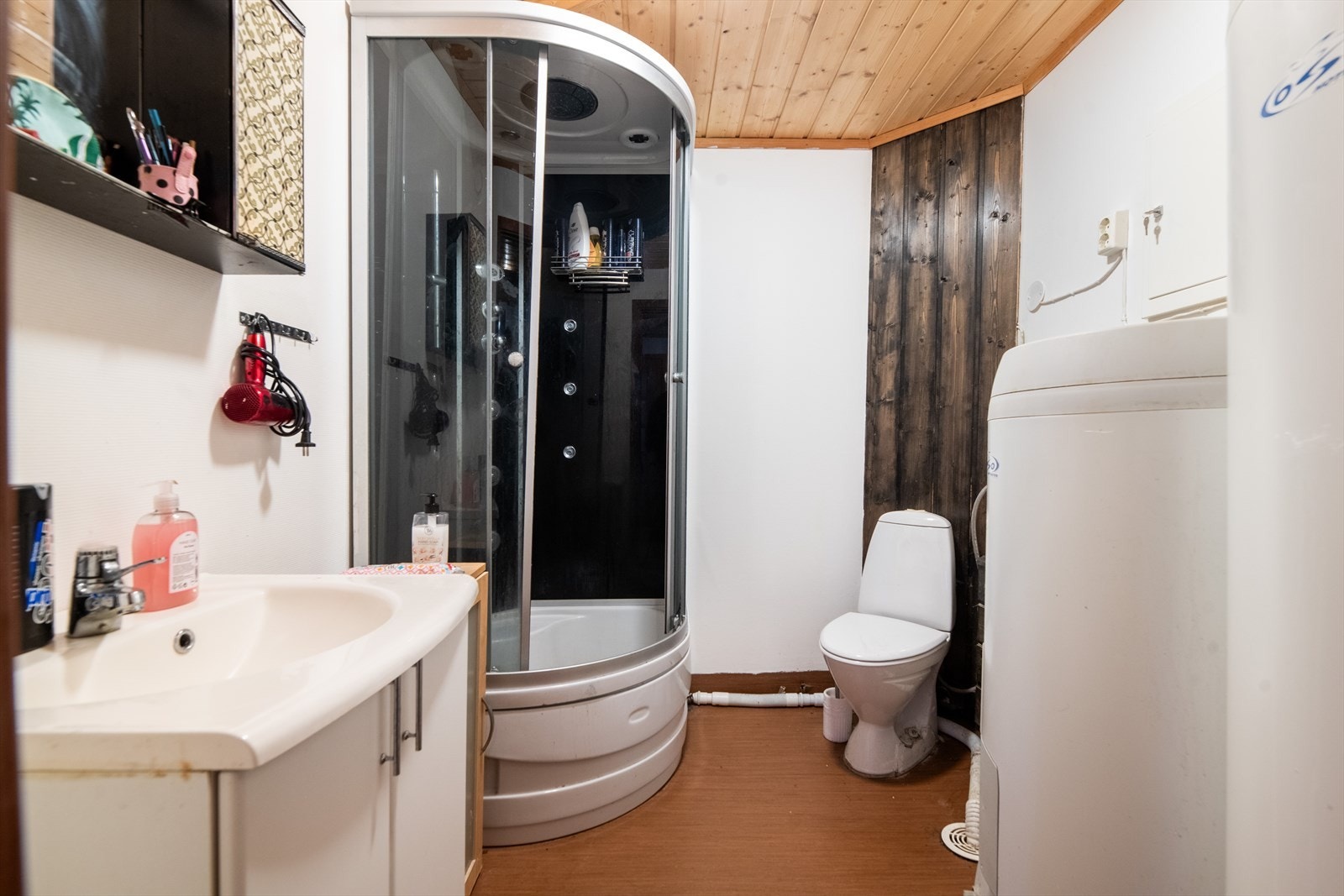 Bad med belegg på gulv og tapet/ panel på vegger. Toalett, dusjkabinett og innredning med heldekkende hvit vask og underskap med slette fronter. Varmekabler, balansert ventilasjon og to varmtvannstanker. Galleribilde