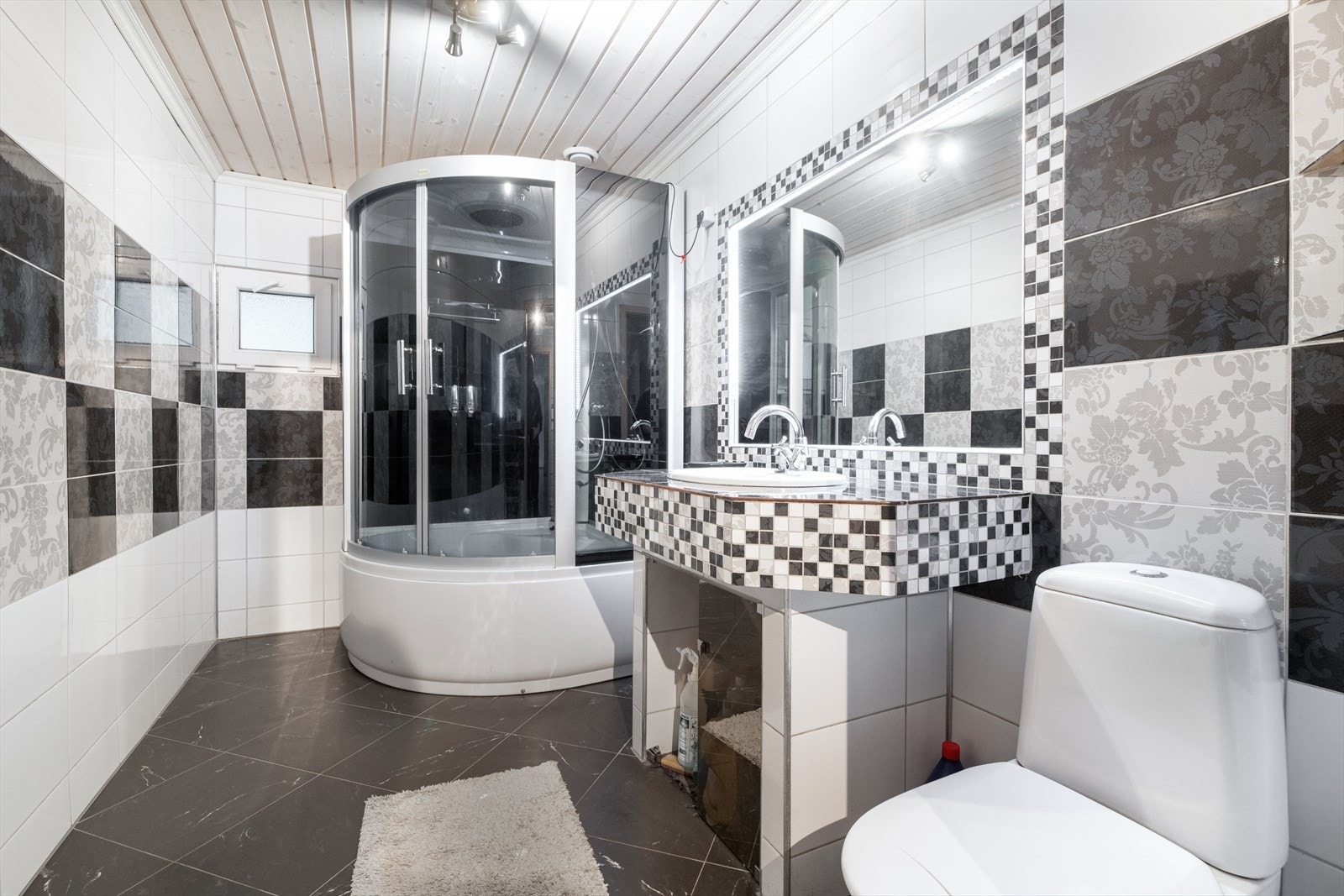 Bad fra 2011/ 2013 med flis på gulv og vegger. Her er det toalett, dusjkabinett og plassbygget innredning med flis, vask og speil. Det er varmekabler i gulv og ventilasjon via ventilasjonssystem. Bygningssakkyndige har bemerkninger på badet. Galleribilde