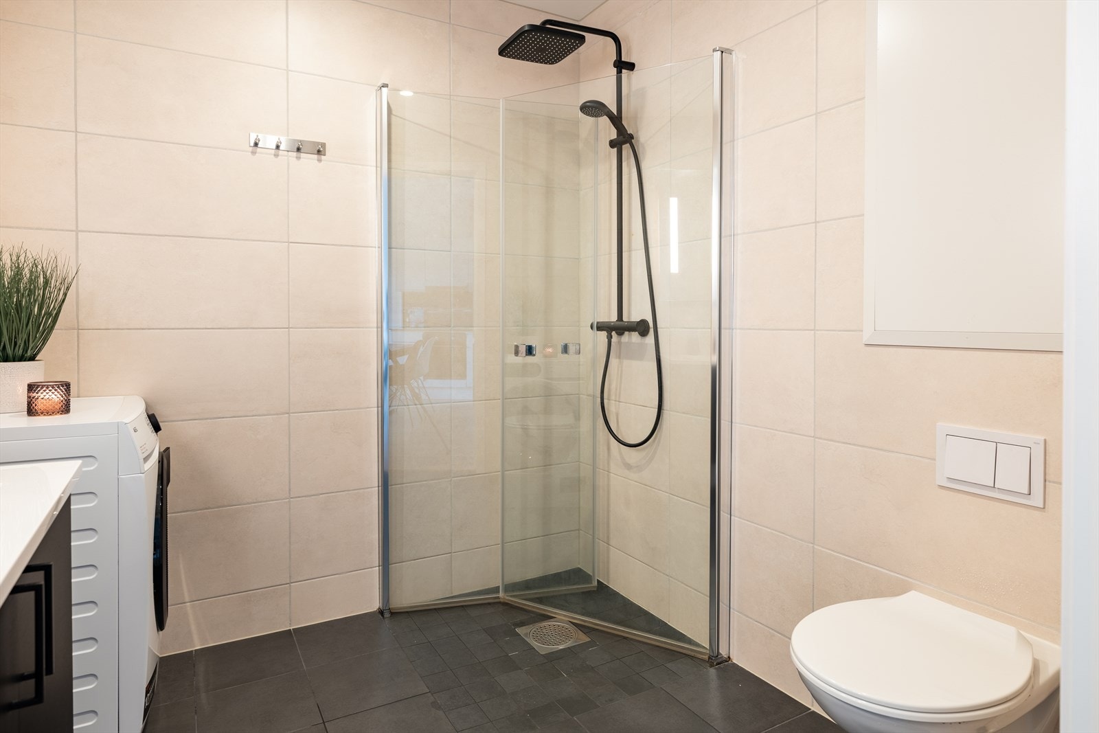 Badet byr på servant, dusjhjørne med innfellbare glassdører og dusjgarnityr montert på vegg, vegghengt toalett og opplegg for vaskemaskin. Galleribilde