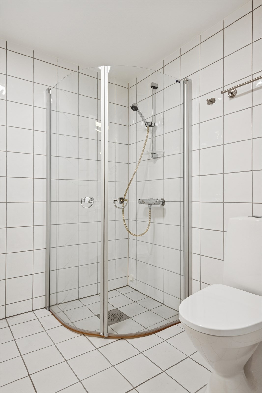 Rommet inneholder dusjhjørne med innfellbare dører, toalett og servantinnredning. Galleribilde