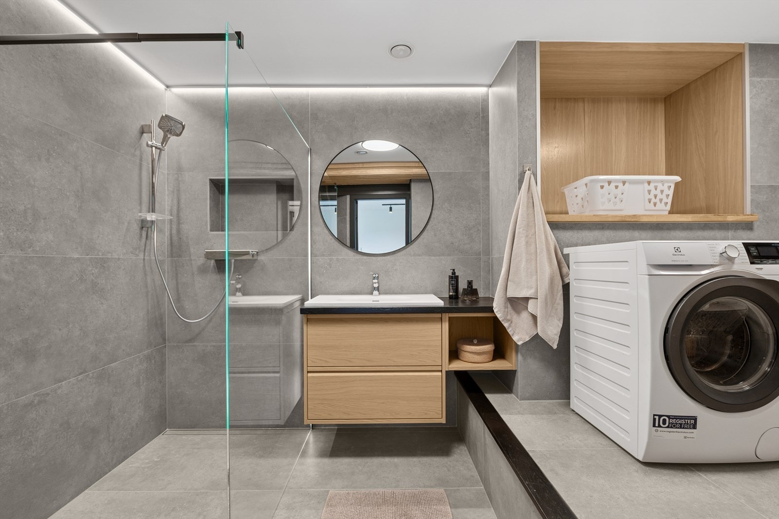 Badet er delikat innredet med store, grå fliser på gulv og vegger. Badet er utstyrt med dusjhjørne, veggehengt toalett og veggseksjon med servant. Vaskerommet har opplegg for vaskemaskin, plass til tørketrommel og varmtvannsbereder på ca. 200 liter. Galleribilde