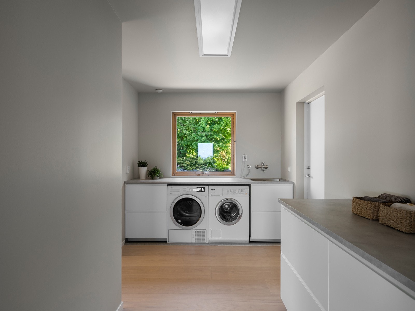 Vaskerommet fungerer også som en praktisk bi-inngang og grovkjøkken, og har 1-stavs parkett på gulvet som gir et helhetlig uttrykk mot resten av boligen. Galleribilde
