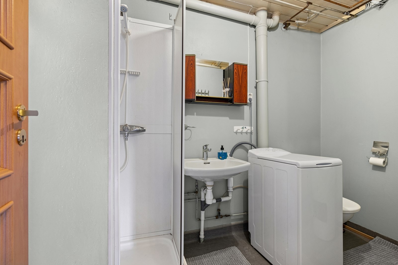 Bad i leilighet i underetasje har etablert vinylbelegg på gulvflater med oppkant på vegg. Malt veggflater i murverk. Det er montert gulvmontert toalett, innredning med heldekkende servanter med ett-hånds armatur og tett dusjkabinett til bad. Galleribilde