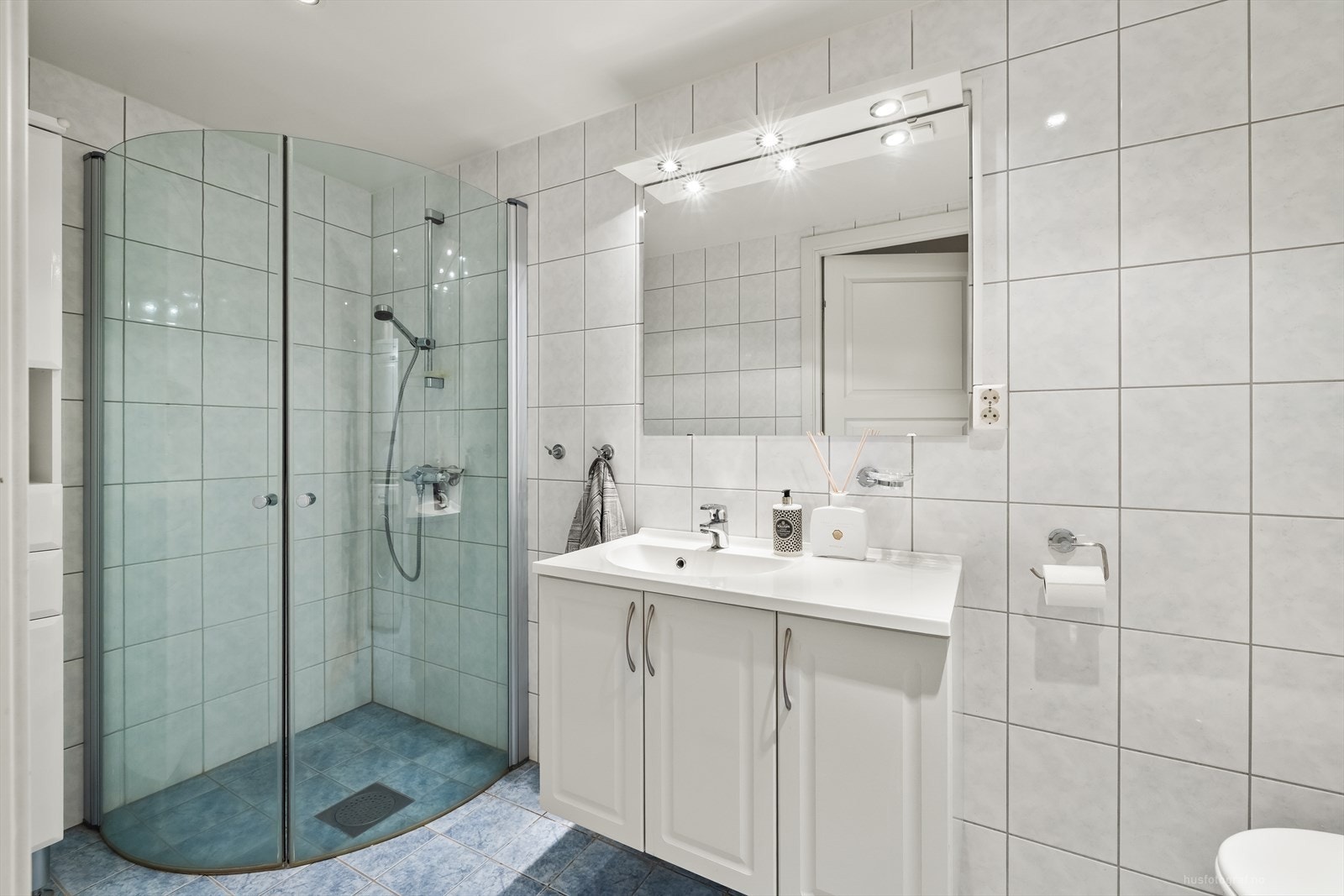 Badet har innredning med nedfelt servant, dusjvegger/hjørne, speil med lys over og praktiske skap under vasken. Galleribilde