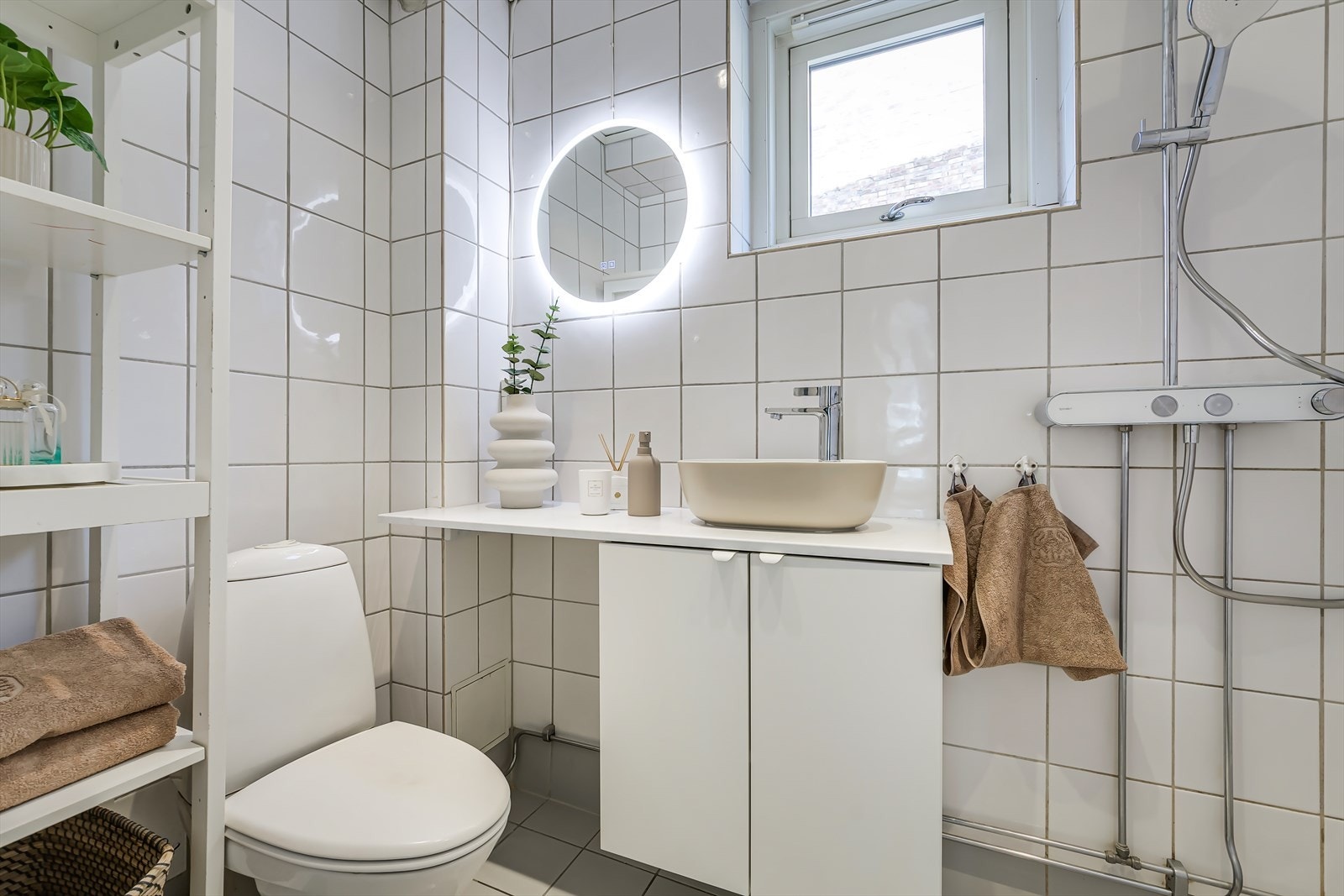 Badet fremstår delikat, med lyse fliser, dusjhjørne, toalett. Galleribilde