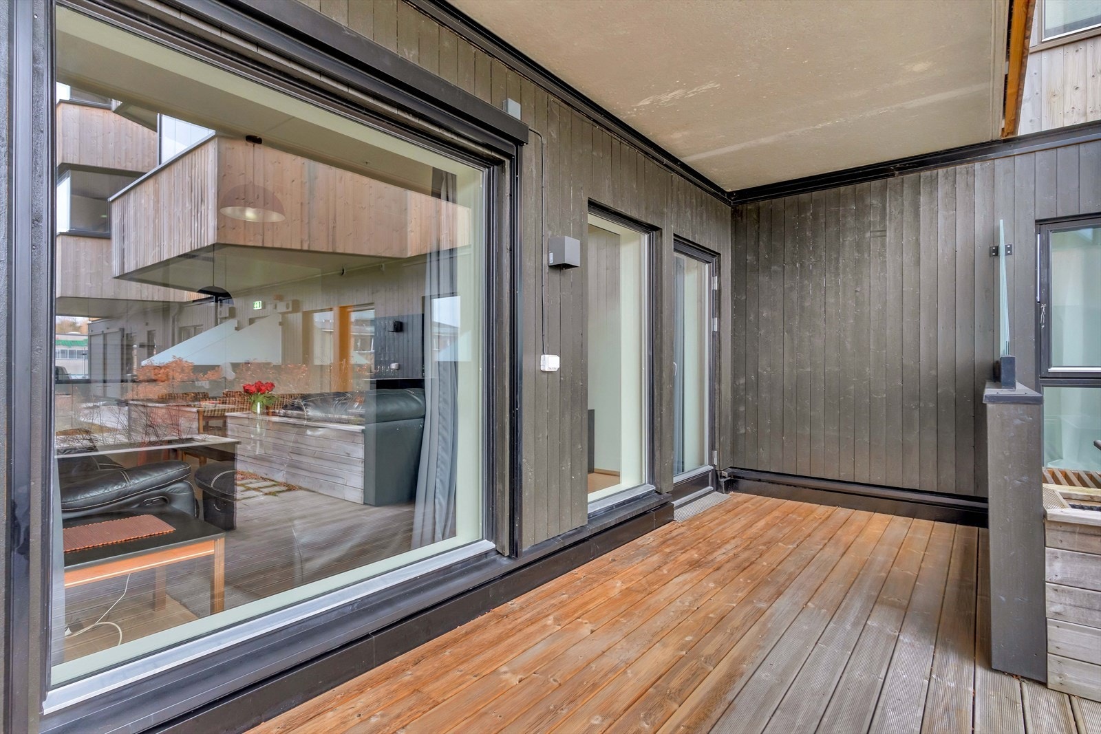 Terrassen fremstår som en lun og koselig sone, omkranset av tett rekkverk, levegger i glass og plassbygget blomsterkasse. Galleribilde