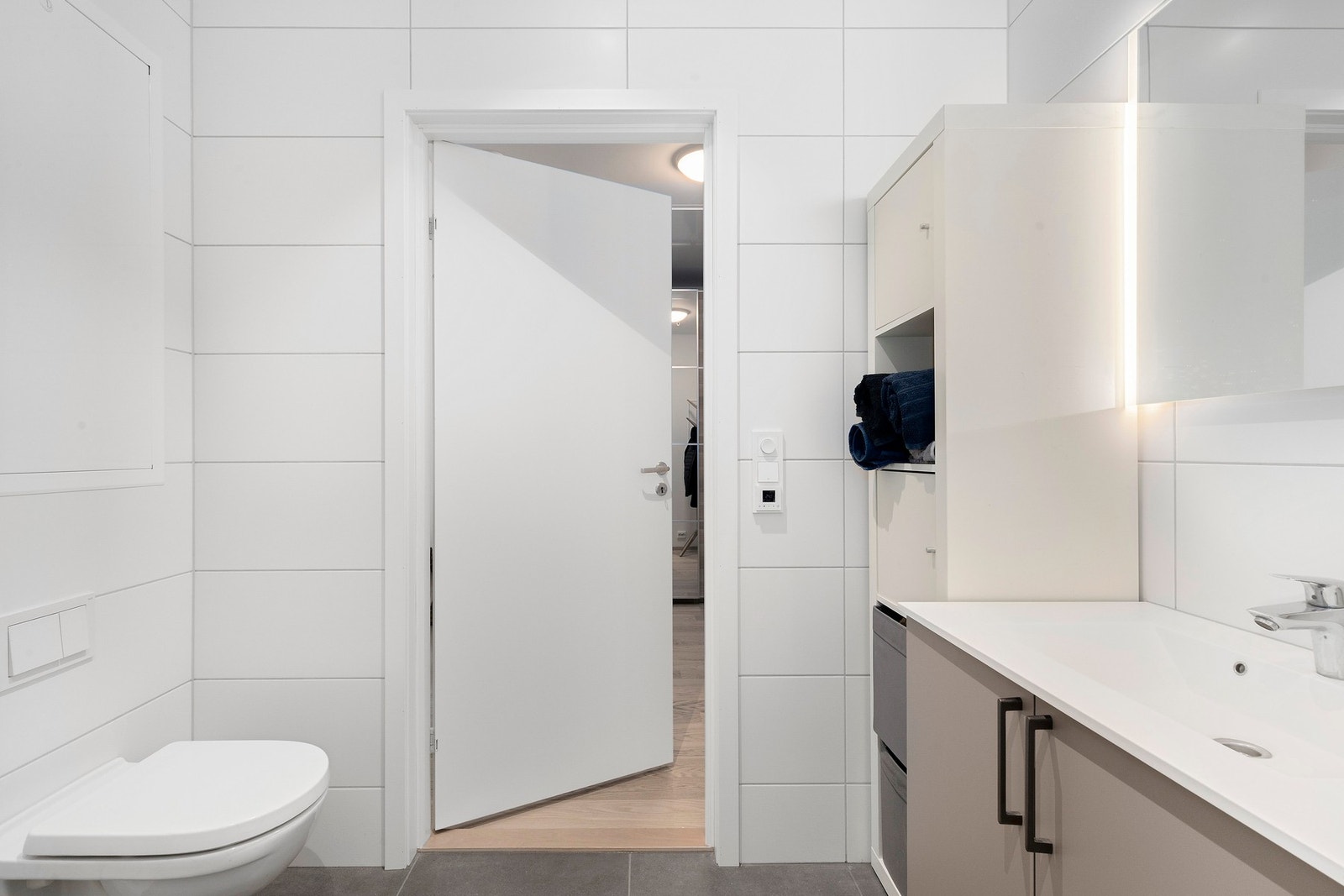 Badet er utstyrt med servantskap, opplegg for vaskemaskin, dusjhjørne med innfellbare dusjdører, veggmontert wc og rørfordelingsskap. Mekanisk avtrekk. Galleribilde