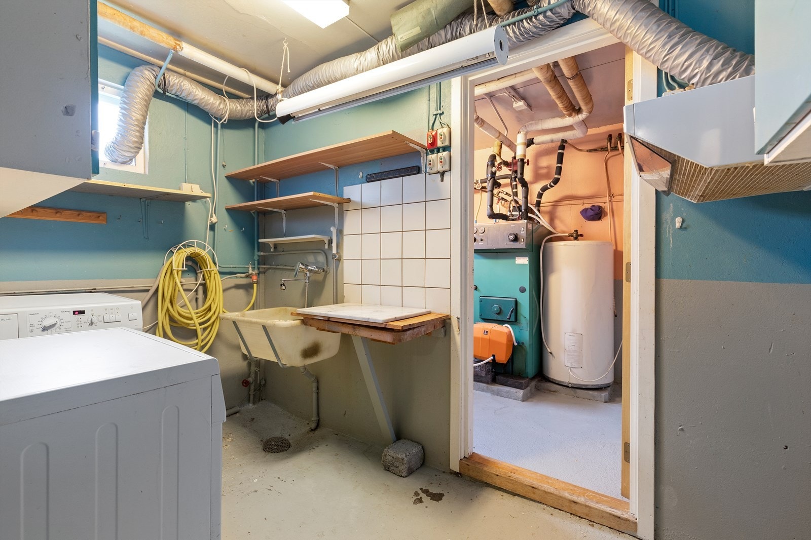 Vaskerommet i underetasjen har betonggulv og malt mur på veggene, samt opplegg for vaskemaskin og vaskekar Galleribilde